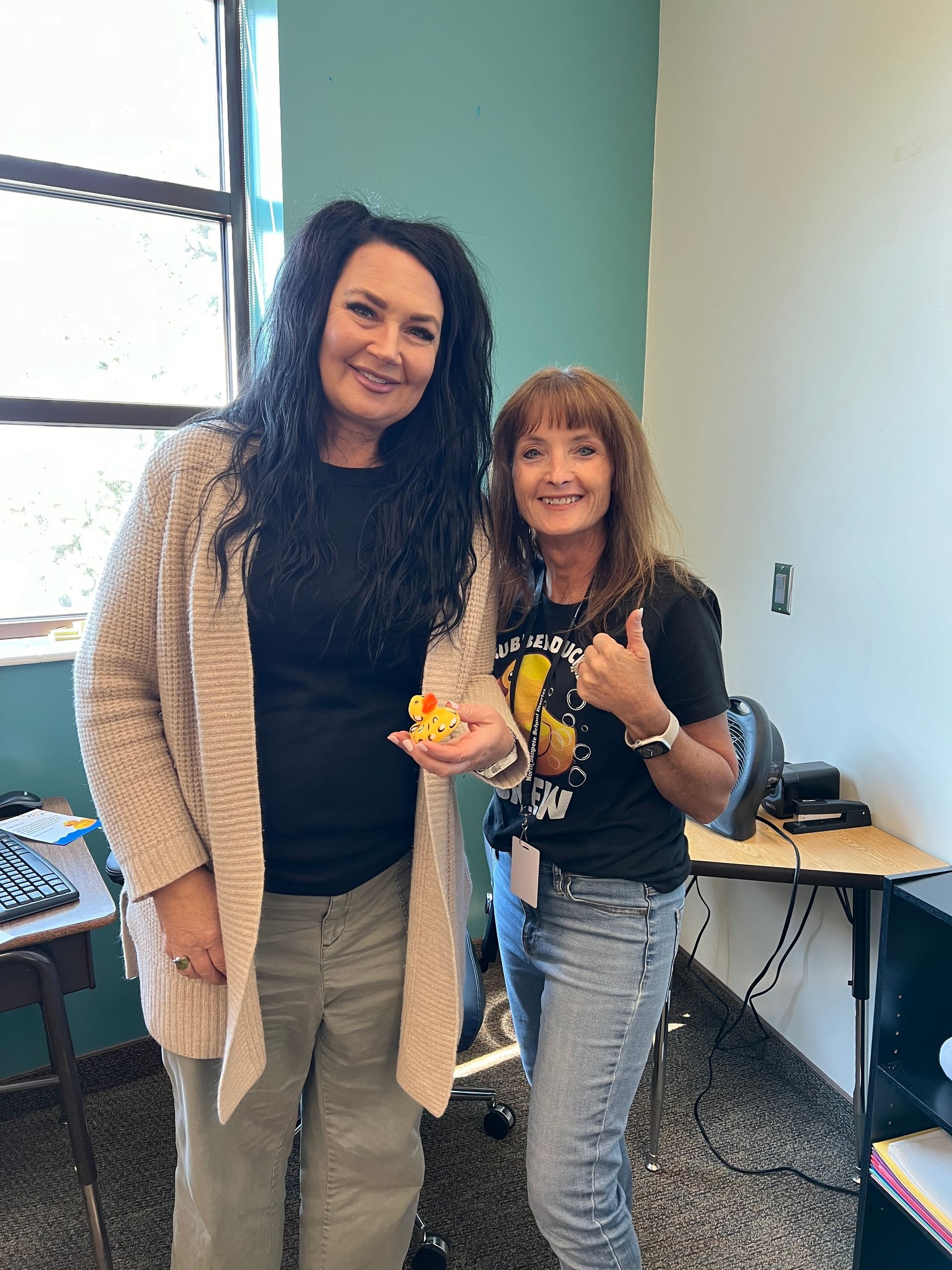 Two women are standing next to each other in a room and one of them is holding a rubber duck.