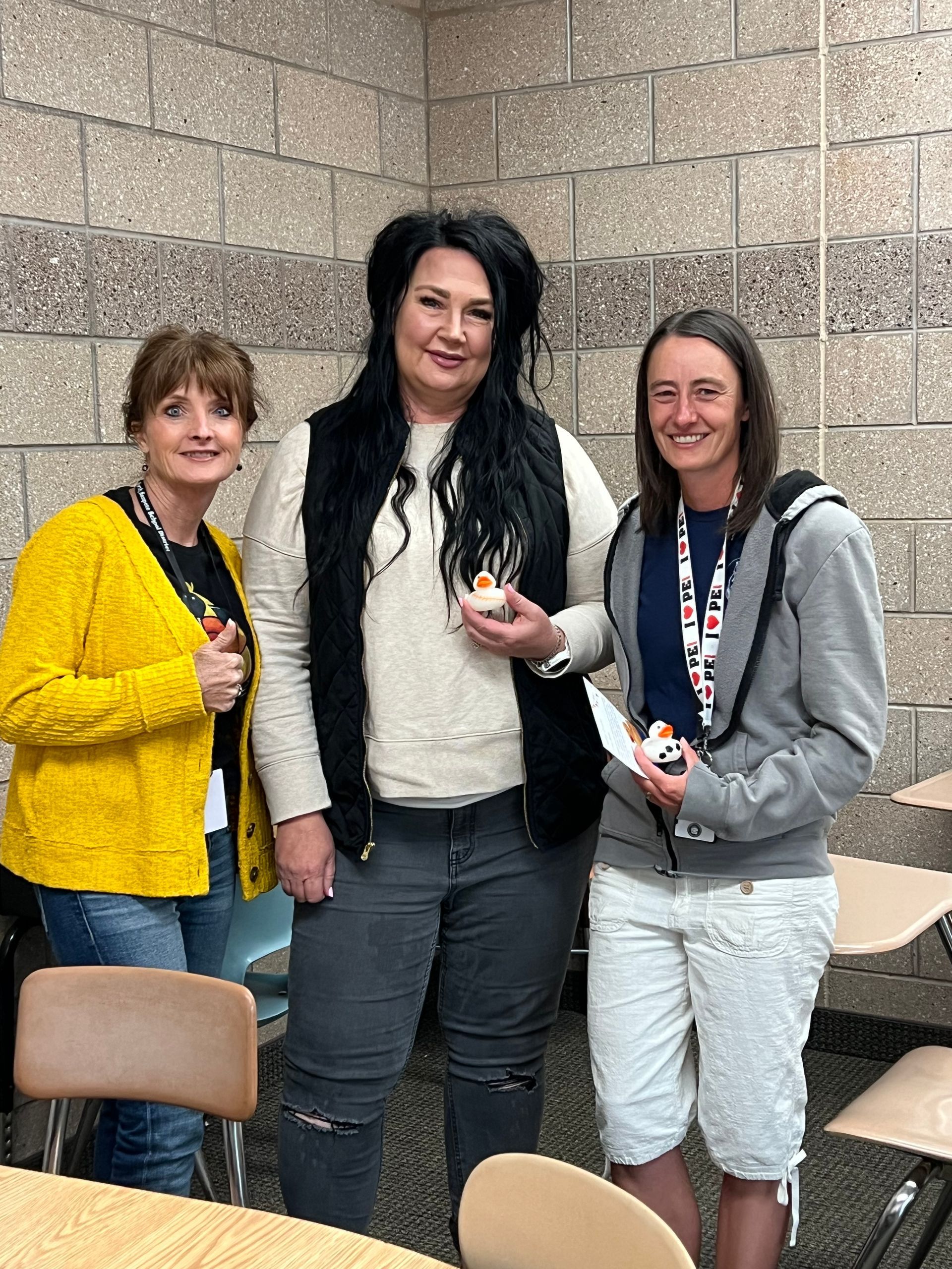 Three women are standing next to each other in a classroom.