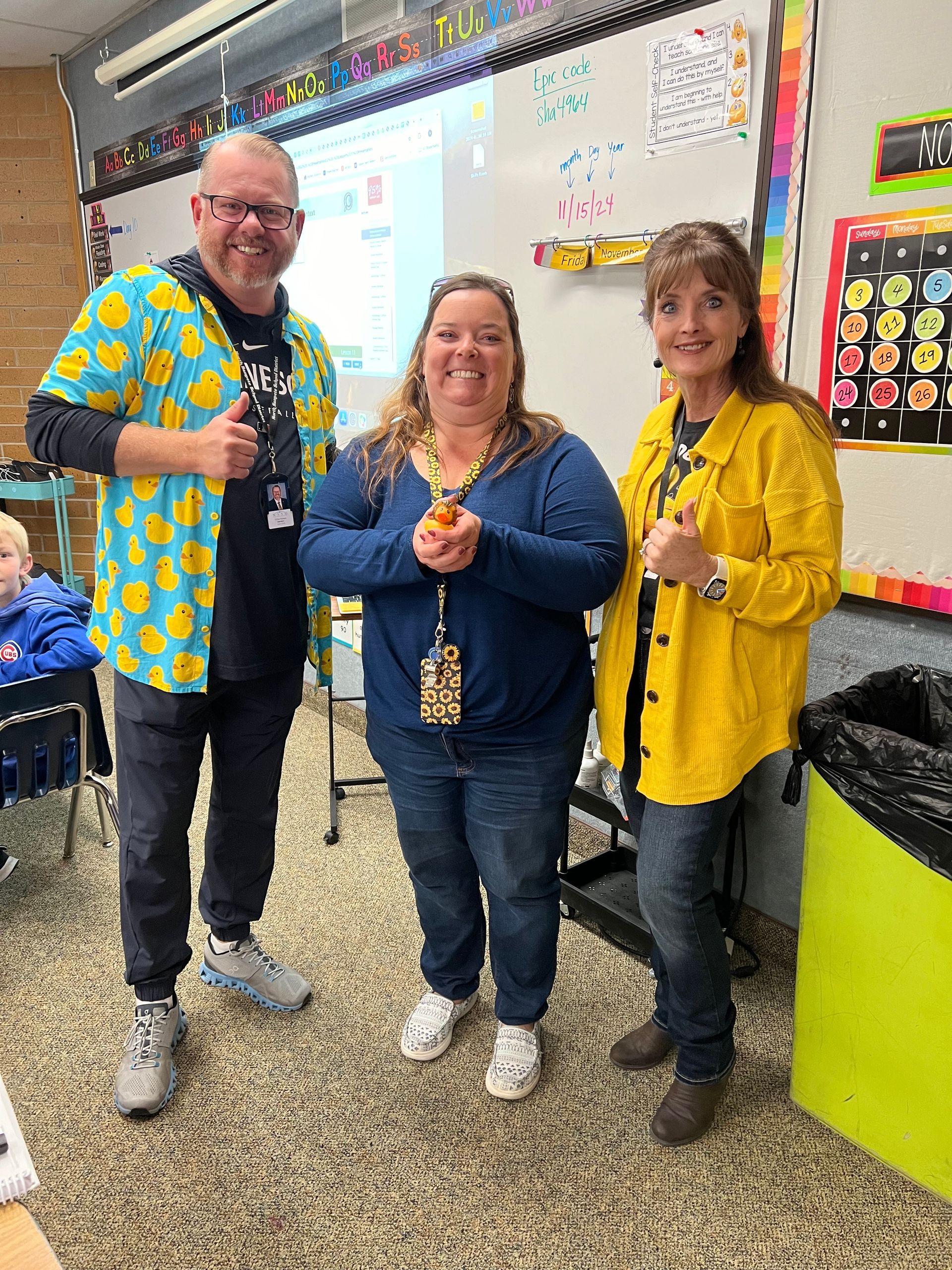 A man and two women are standing next to each other in a classroom.