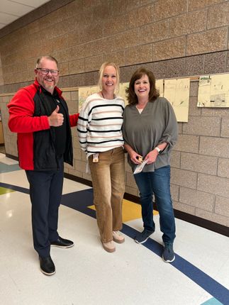 Three people standing in a hallway, one giving a thumbs-up and all smiling.