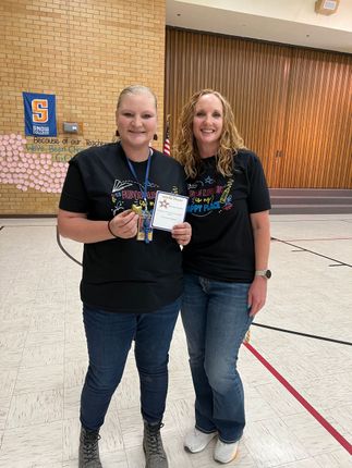 Two women in black shirts holding a trophy and certificate in a gymnasium