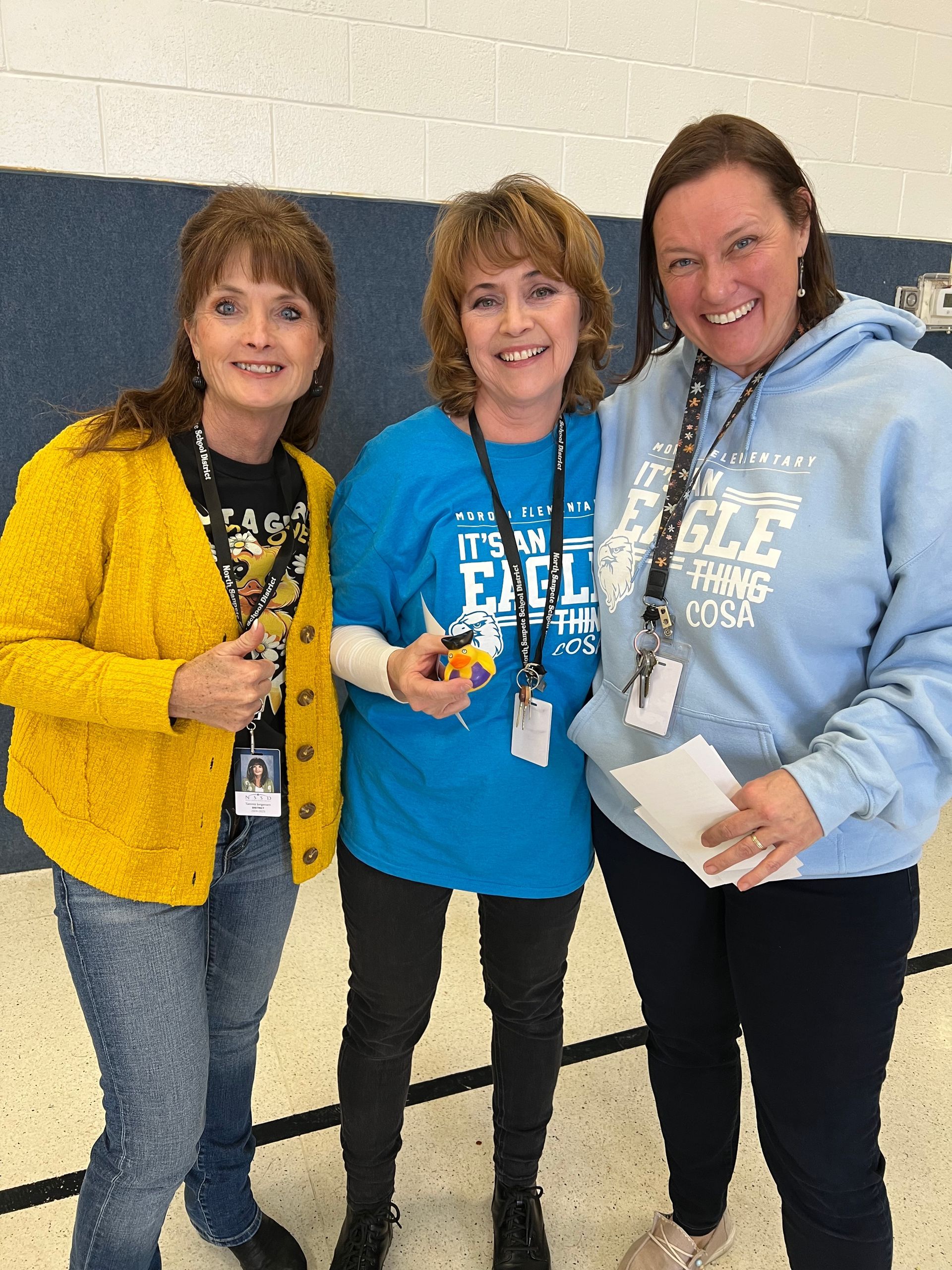 Three women are posing for a picture and one of them is wearing a blue shirt that says eagle