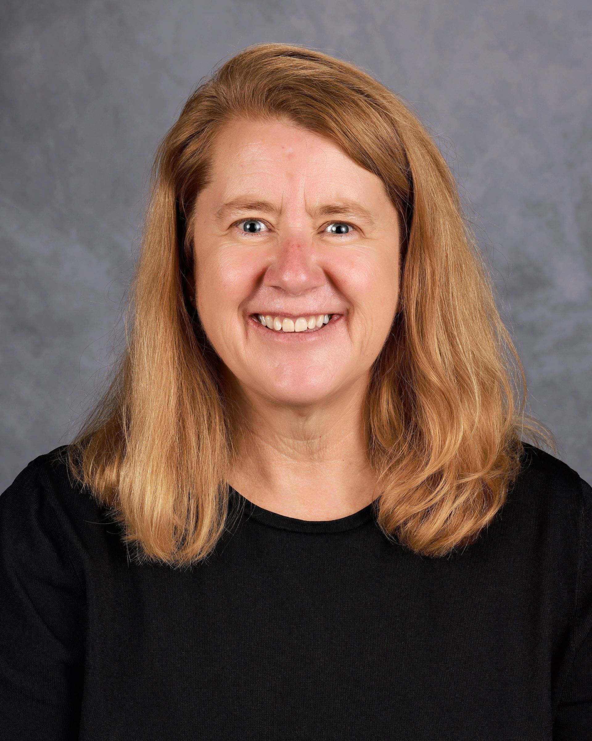 A woman with long blonde hair is wearing a black sweater and smiling for the camera.