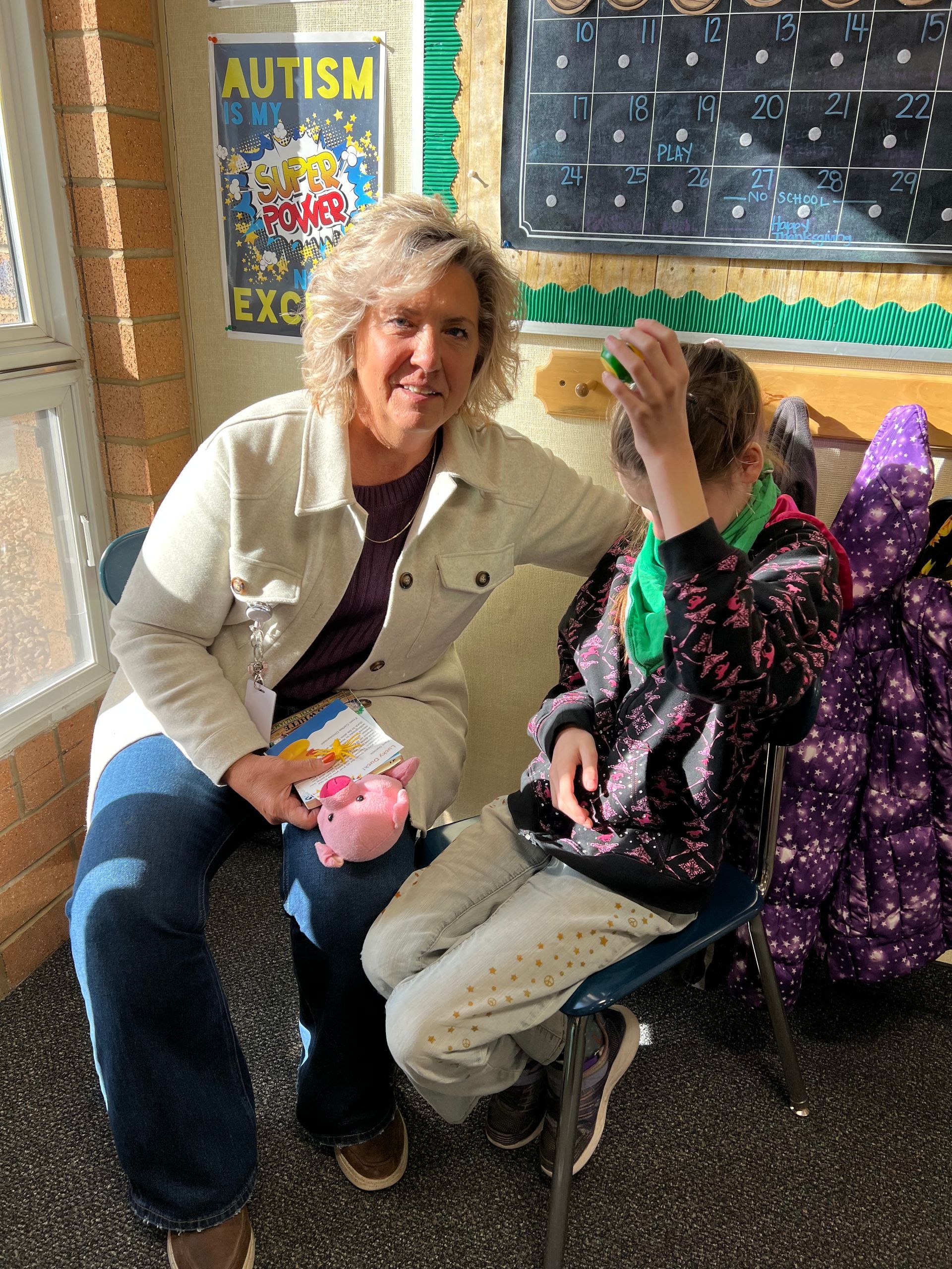 A woman is sitting next to a child with autism in a classroom.