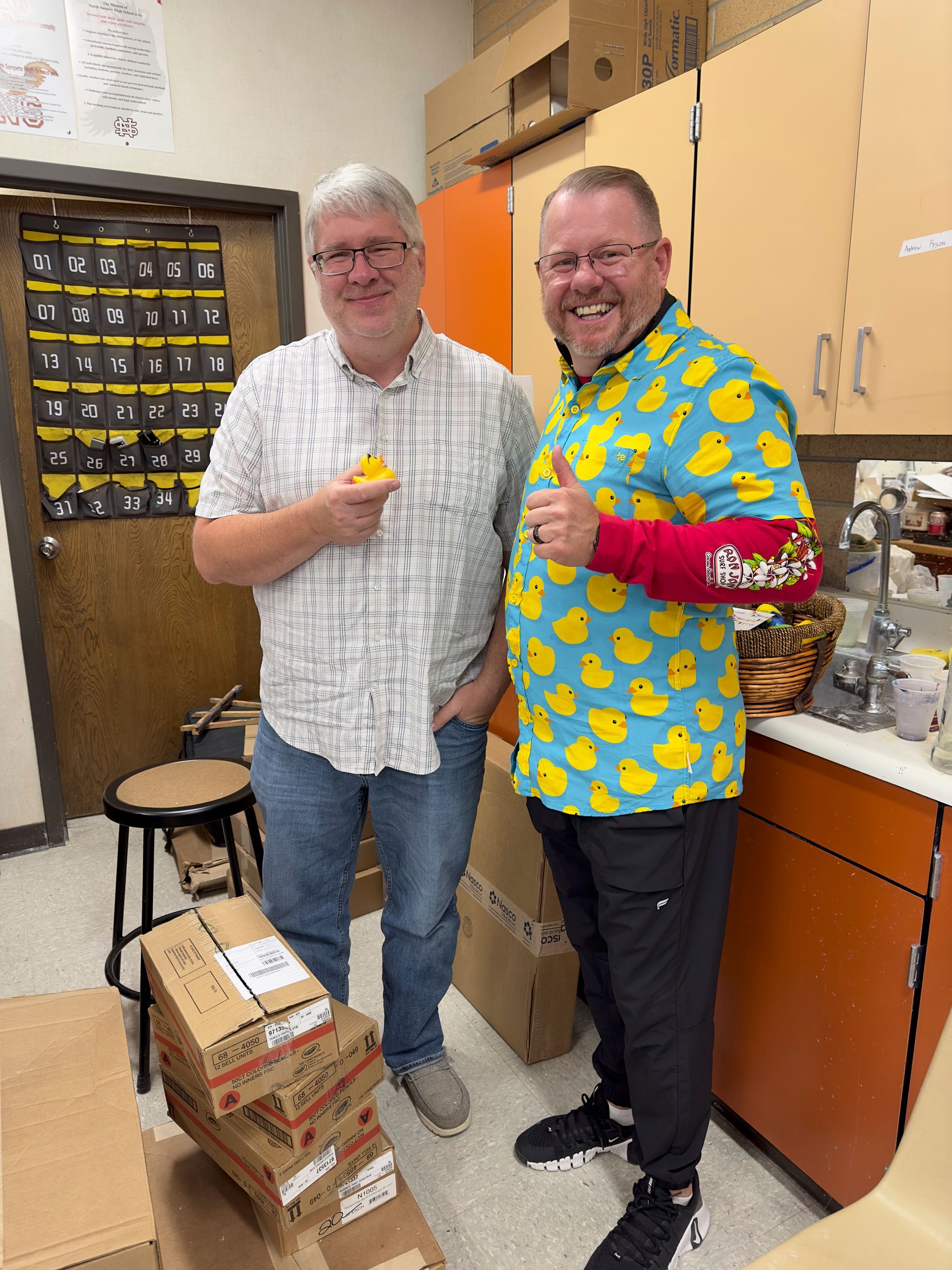 Two men are standing next to each other in a kitchen wearing shirts with ducks on them.