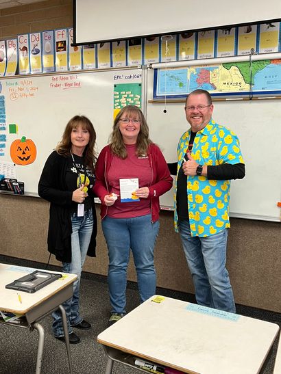 Three people are standing in front of a whiteboard in a classroom.