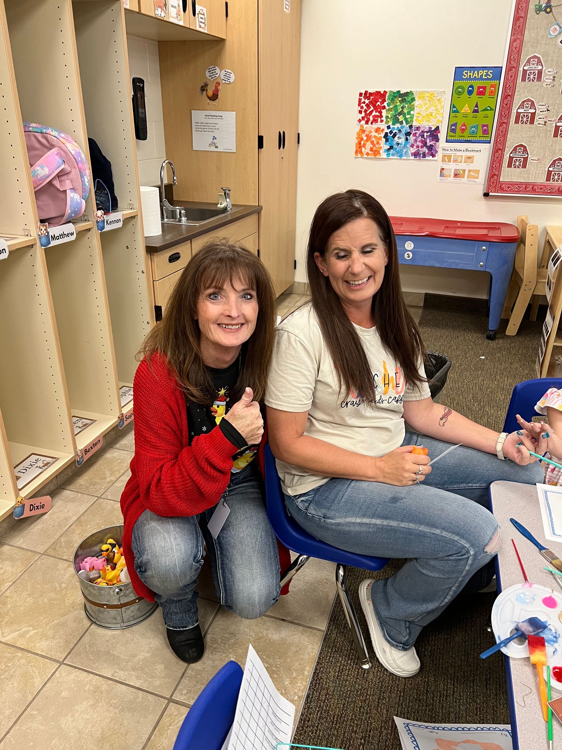 Two women are sitting next to each other in a classroom and smiling.