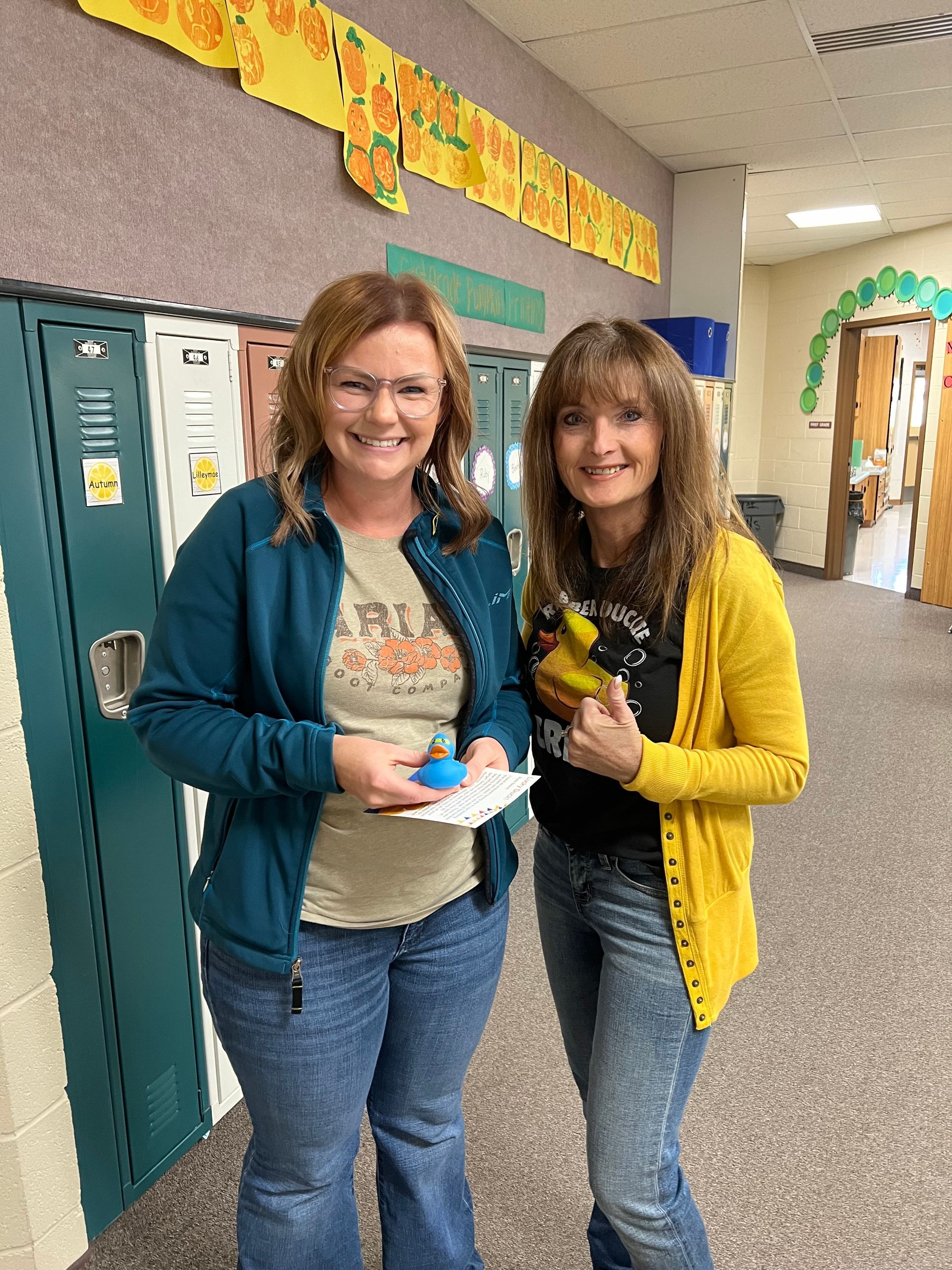 Two women are standing next to each other in a hallway in front of lockers.