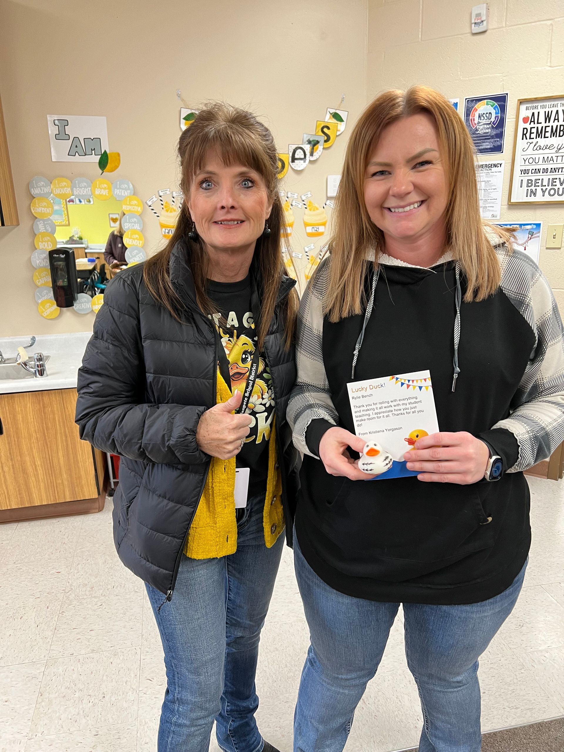 Two women are standing next to each other in a room holding a card.