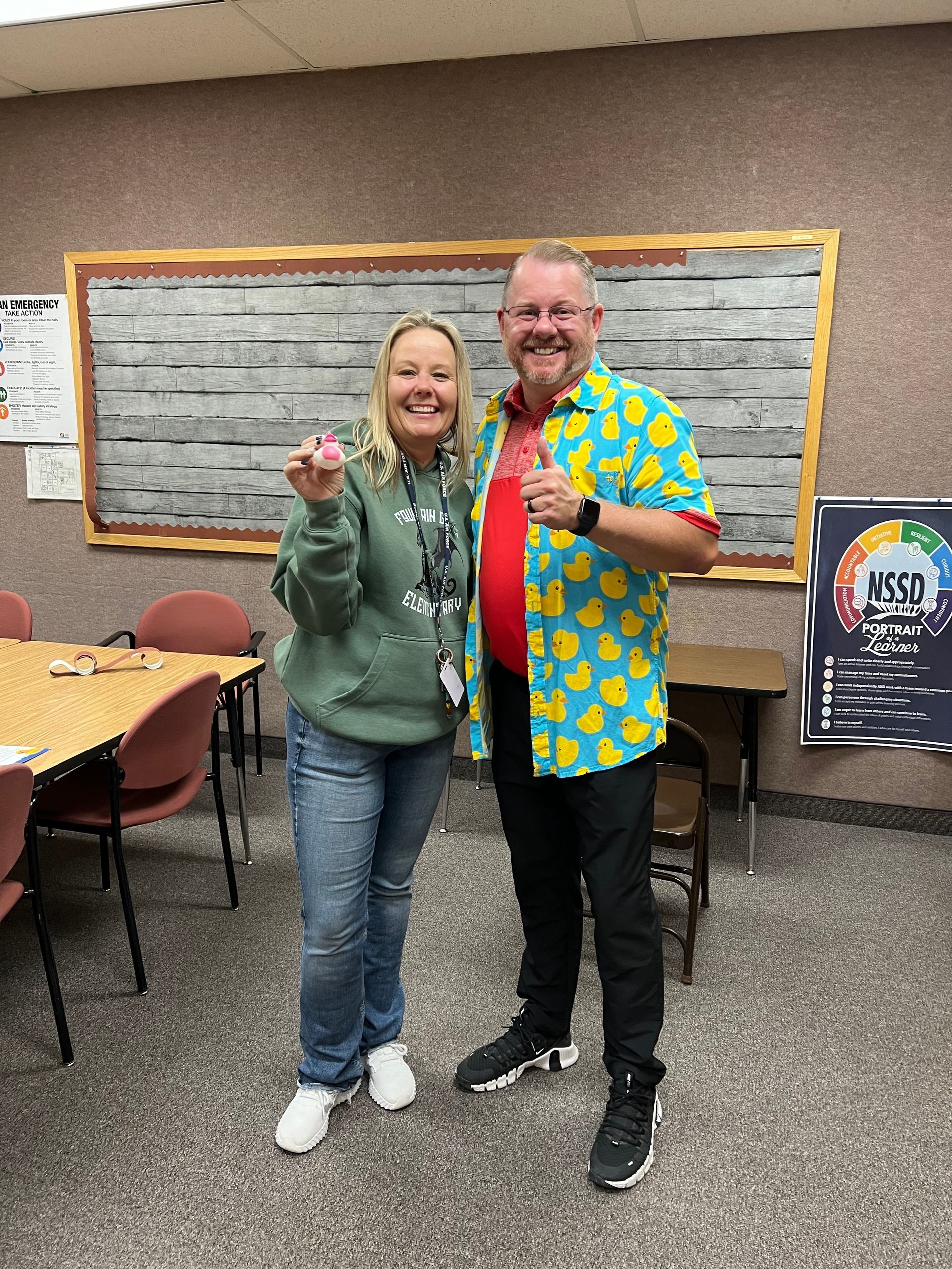 A man and a woman are standing next to each other in a classroom.