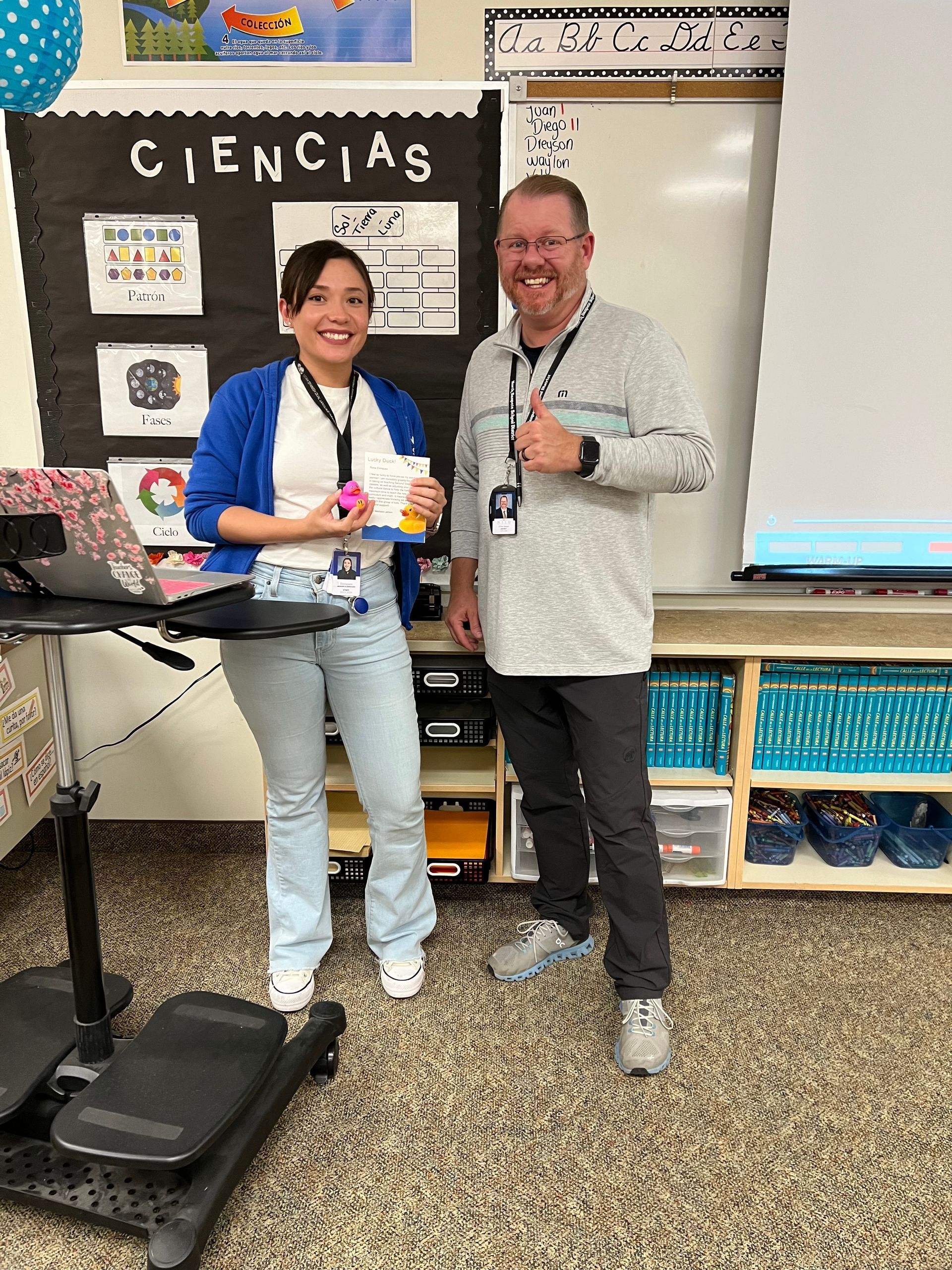 A man and a woman are standing next to each other in a classroom.