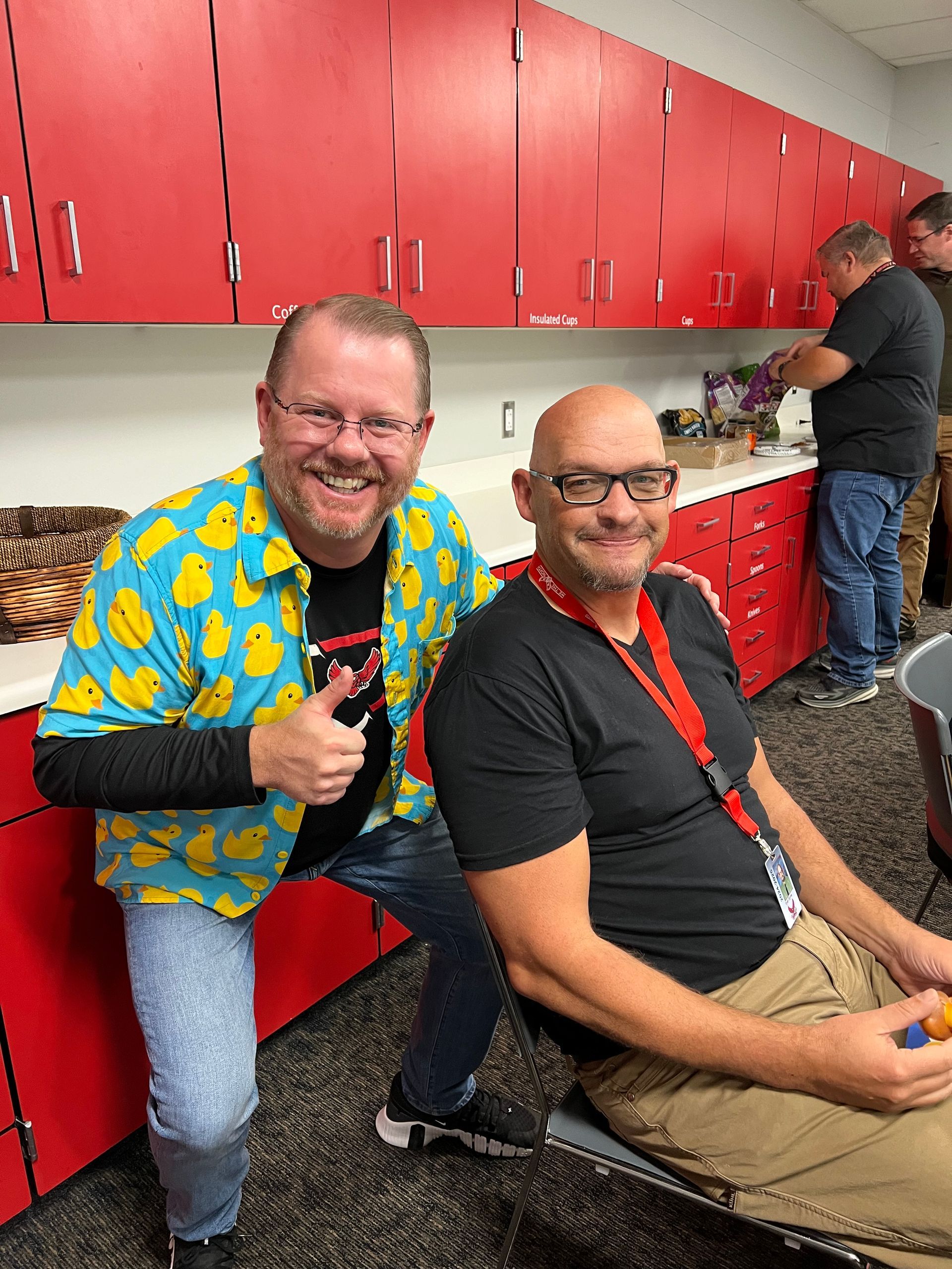 Two men are posing for a picture in a kitchen with red cabinets.