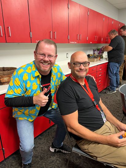 Two men are posing for a picture in a kitchen with red cabinets.