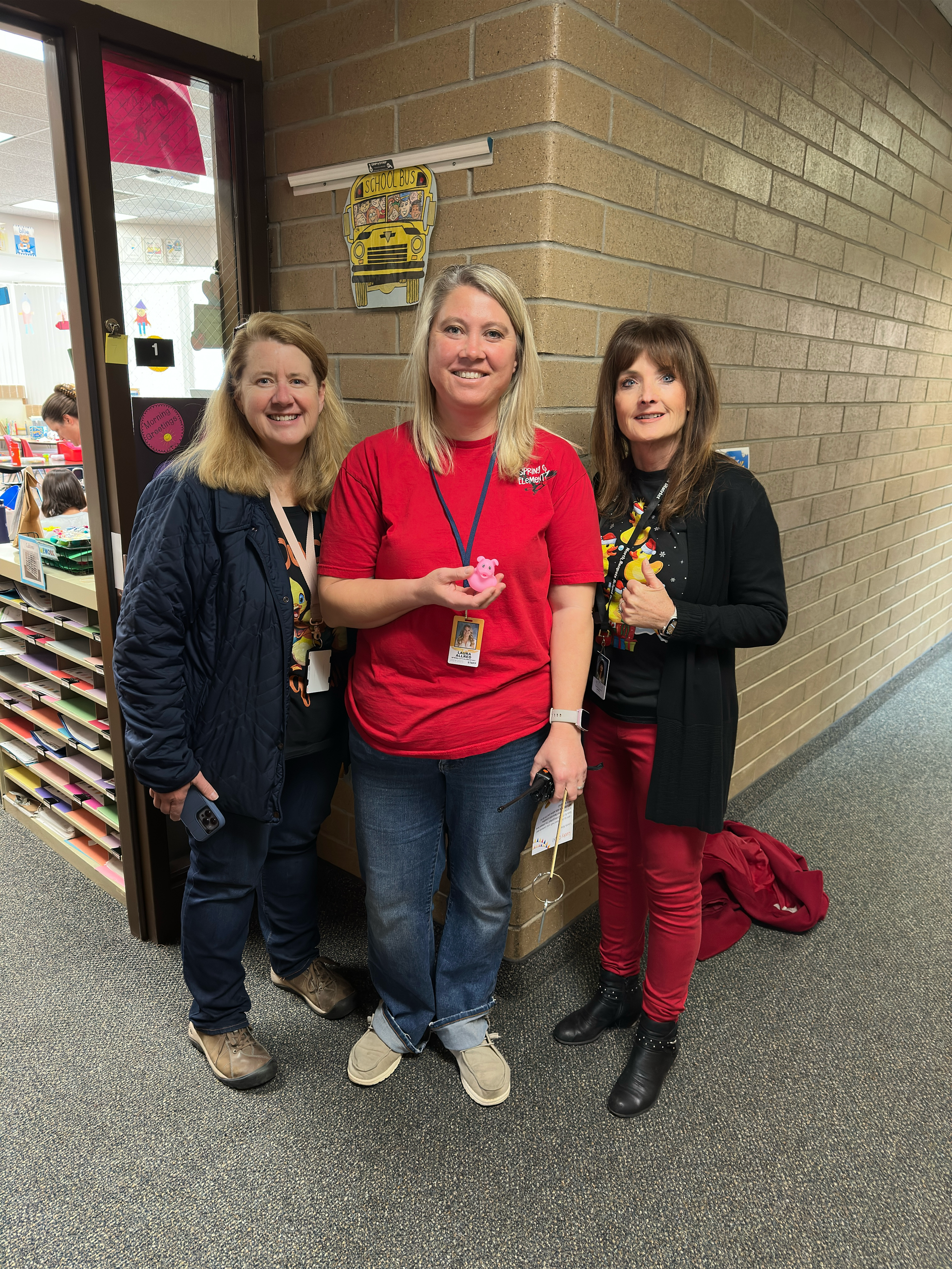 Three women are standing next to each other in a hallway.