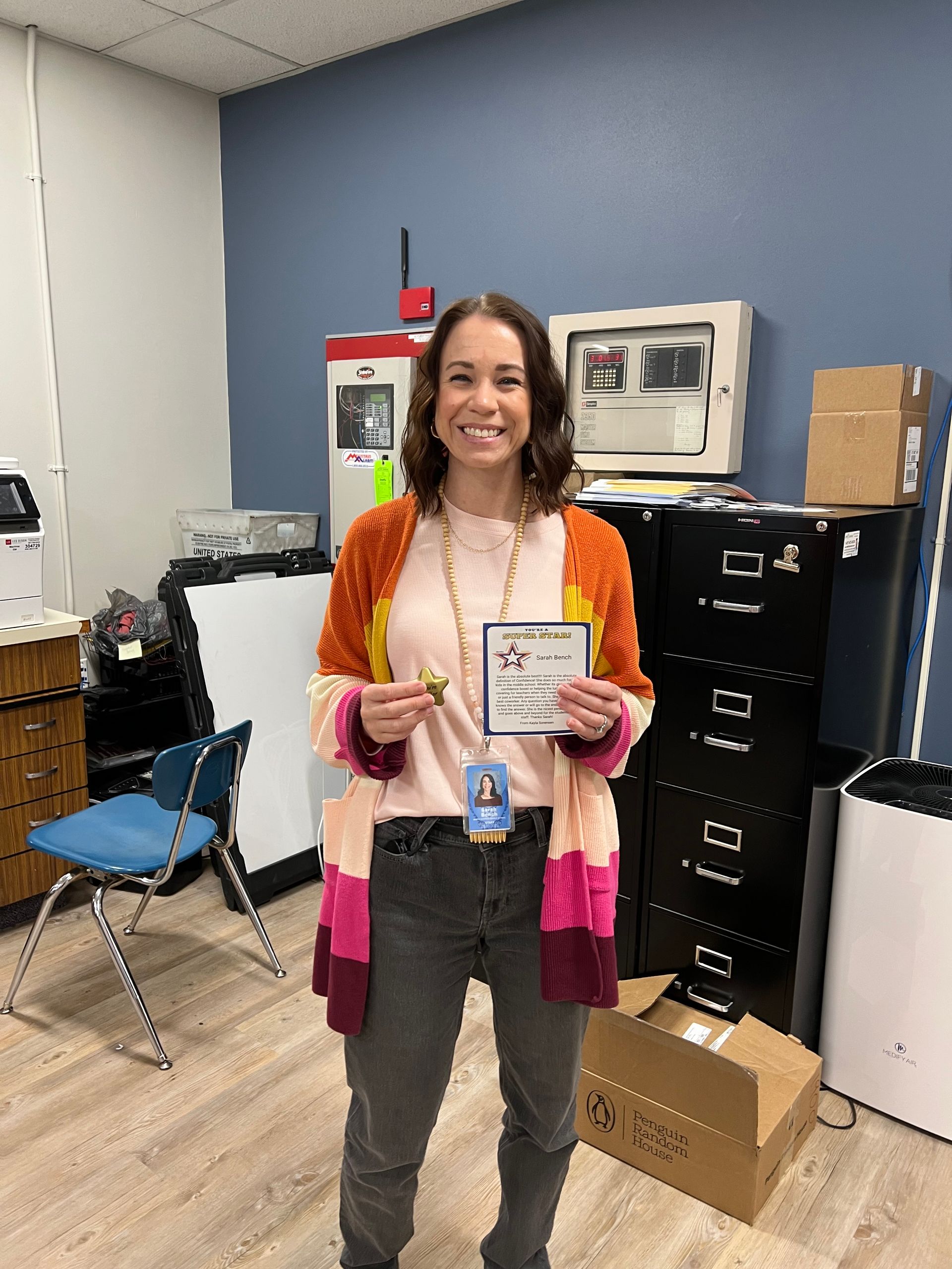 A woman standing in a office wearing a pink sweater smiling.