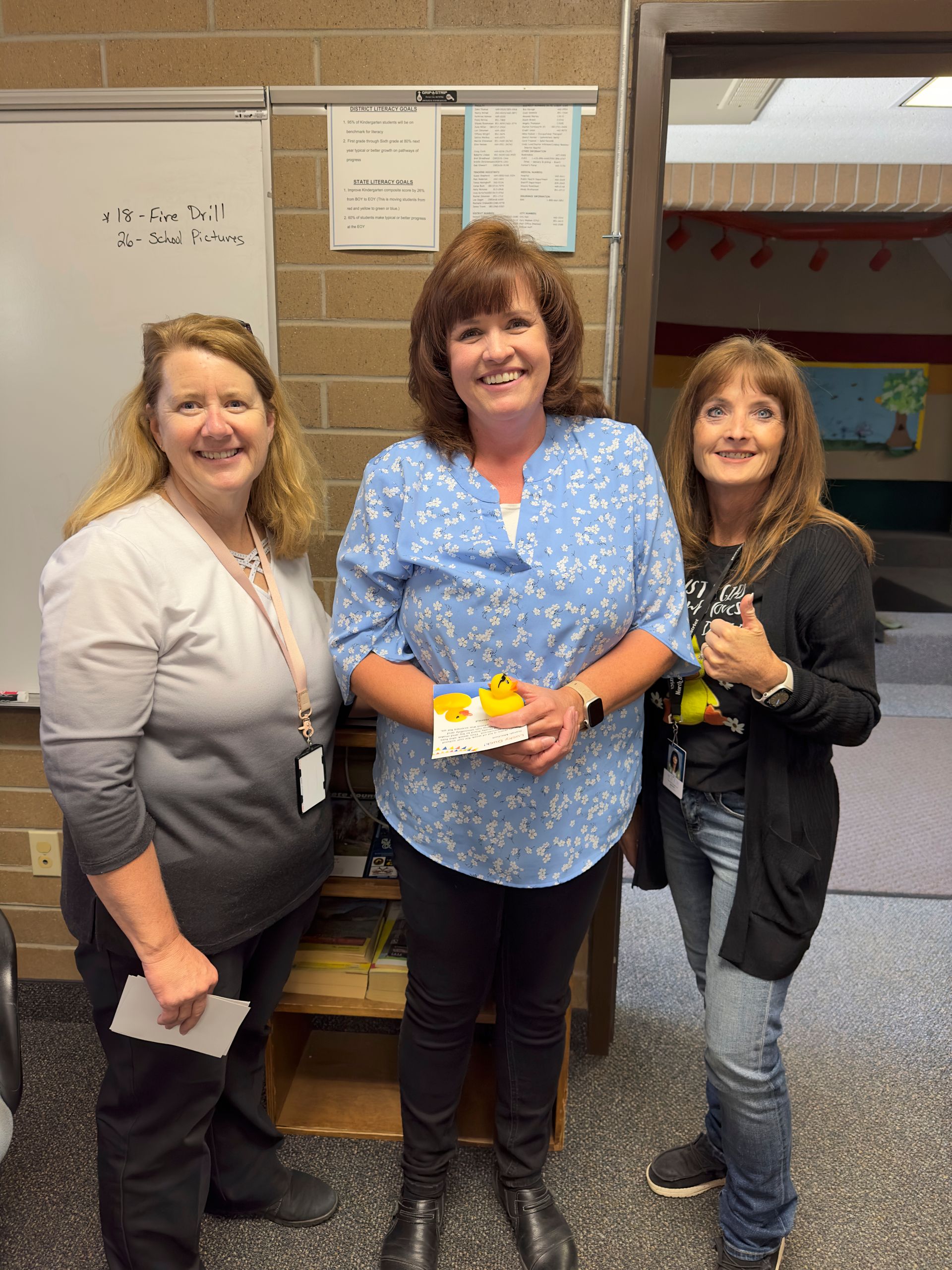 Three women are standing next to each other in a classroom.