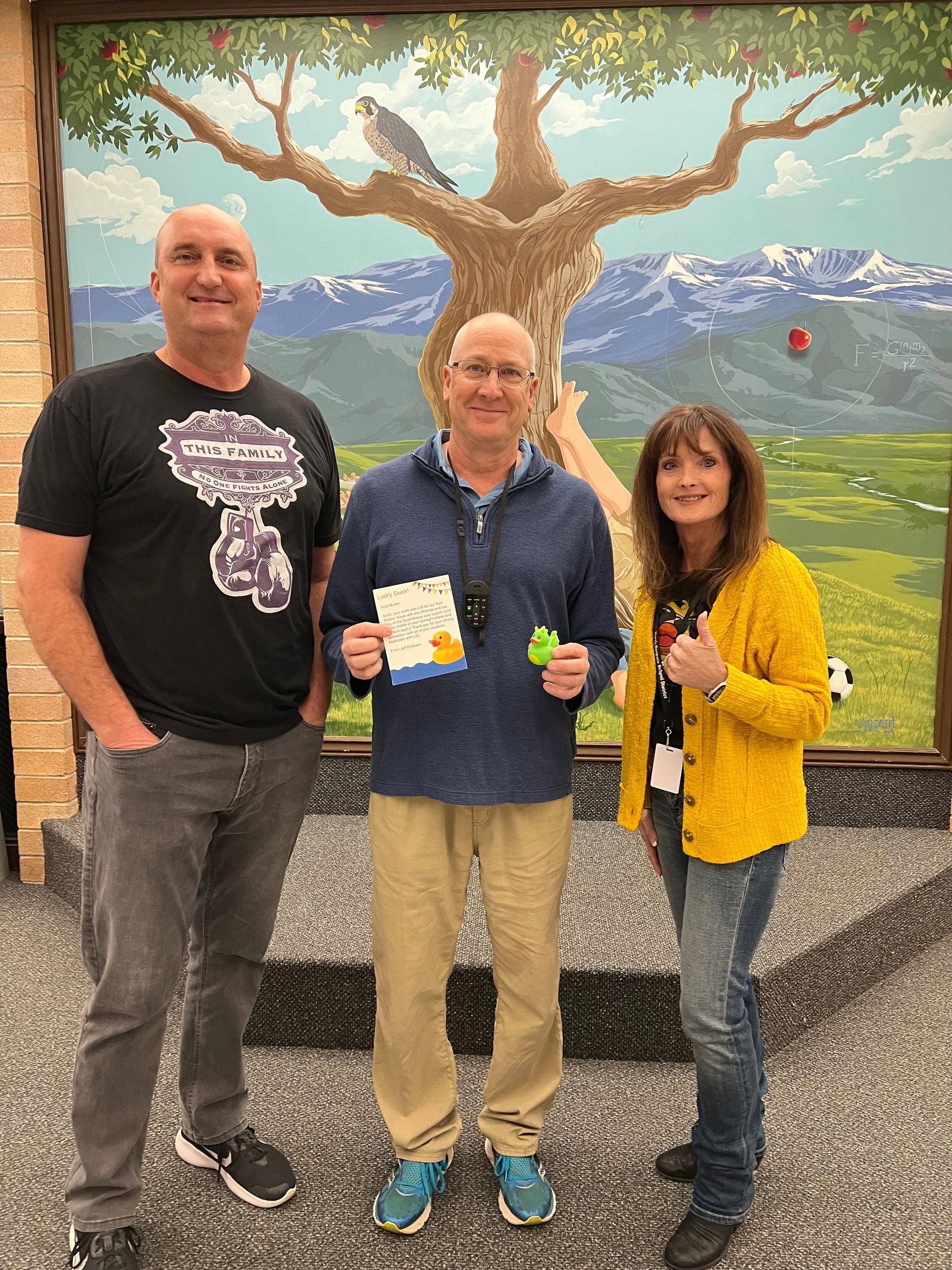 Three people are standing in front of a painting of a tree.