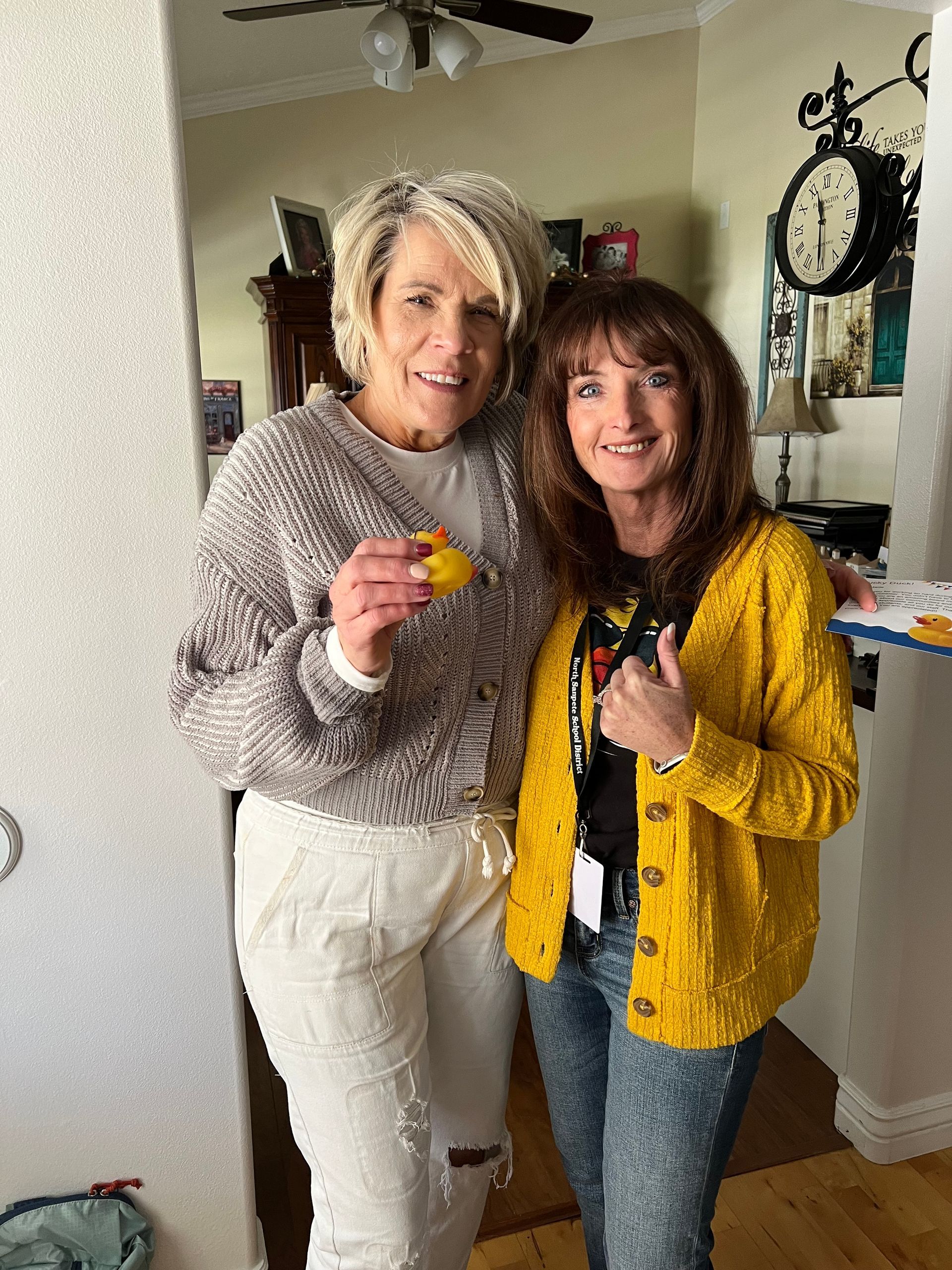 Two women are posing for a picture in a living room . one of the women is wearing a yellow cardigan.