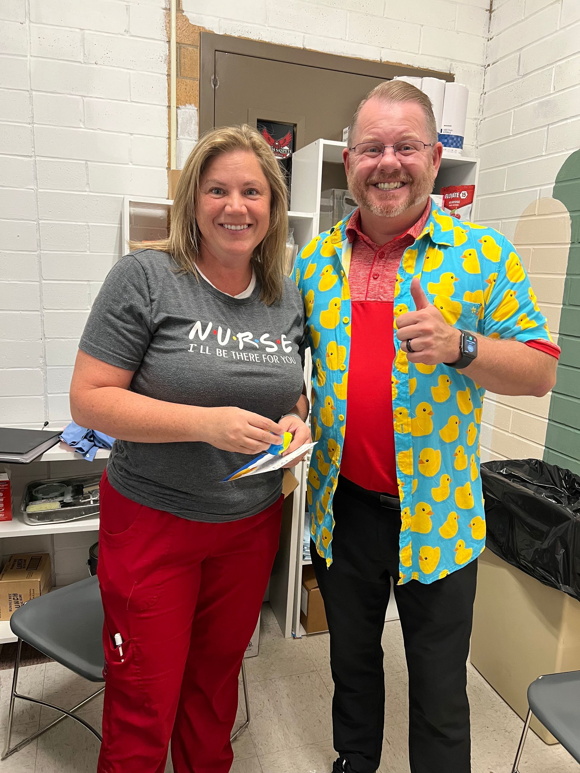 A man and a woman are standing next to each other in a room . the man is wearing a duck shirt.