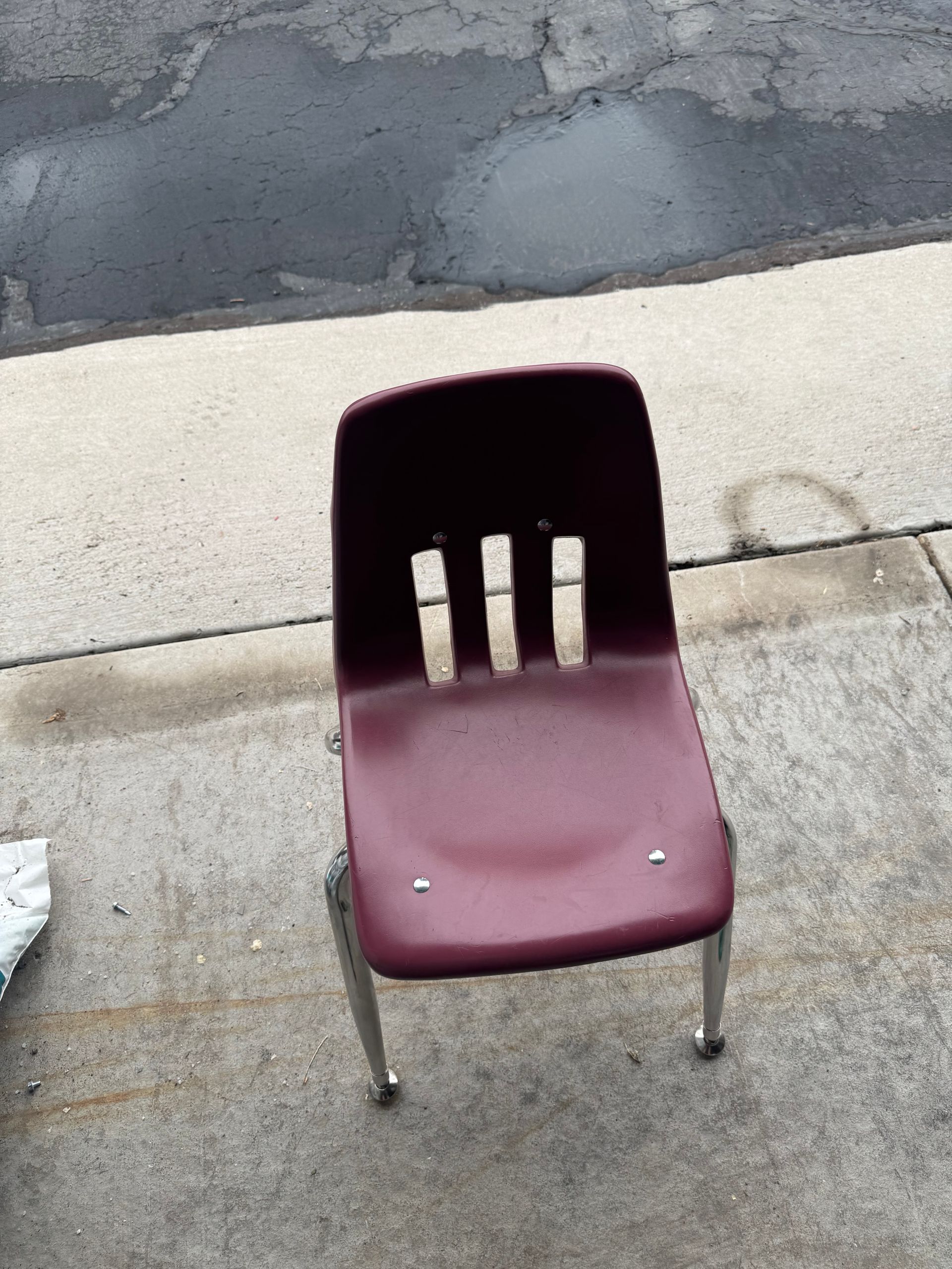 Burgundy plastic school chair on a concrete surface.