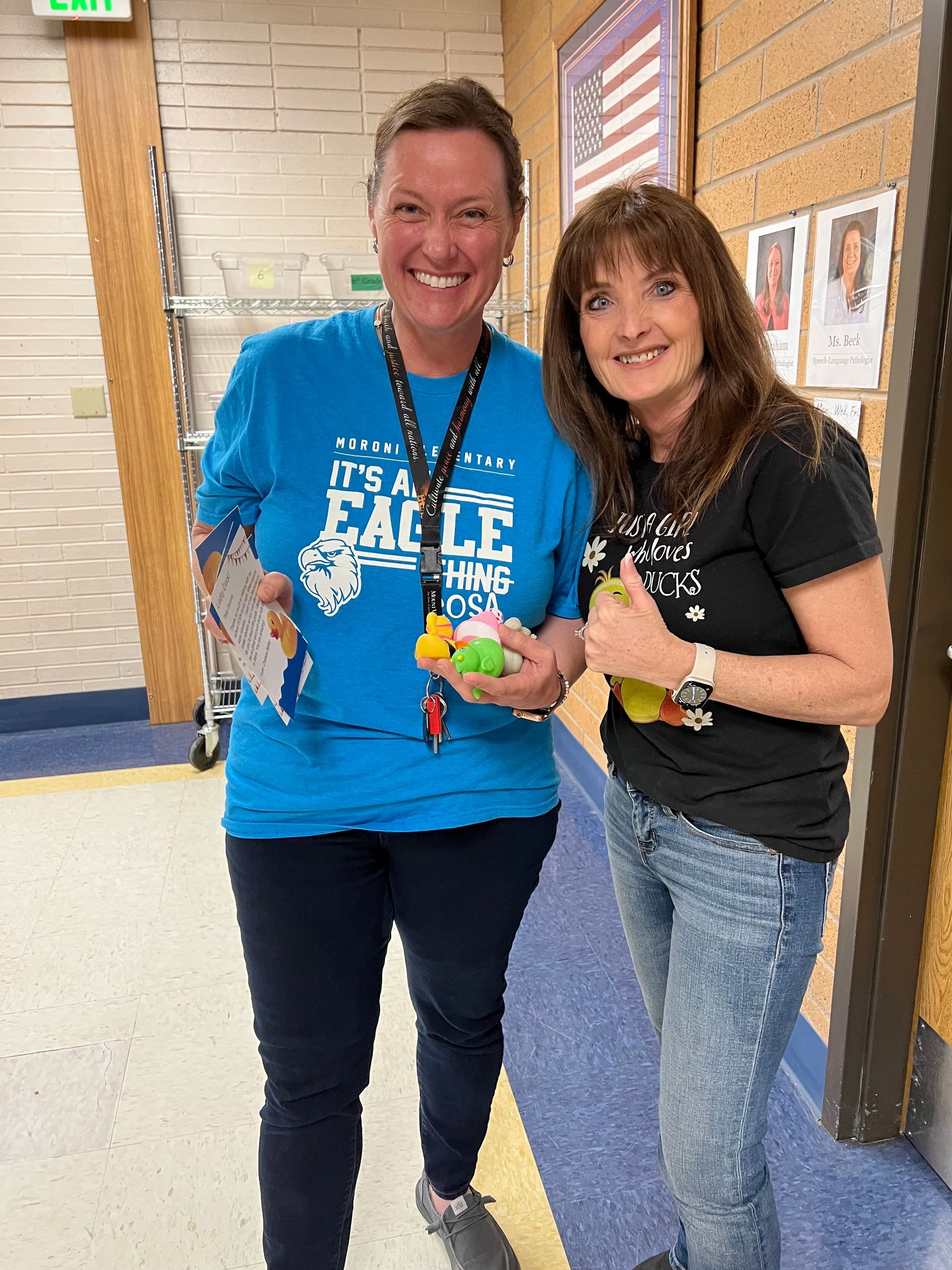Two women are standing next to each other in a hallway holding toys.