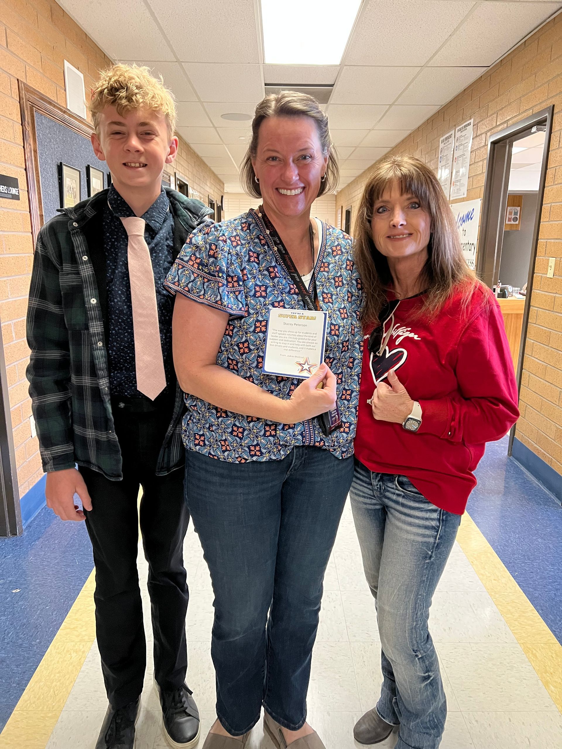 Three people standing in a school hallway, smiling and holding a certificate.