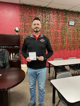 Man holding a certificate in a room with red floral wall decor and tables.