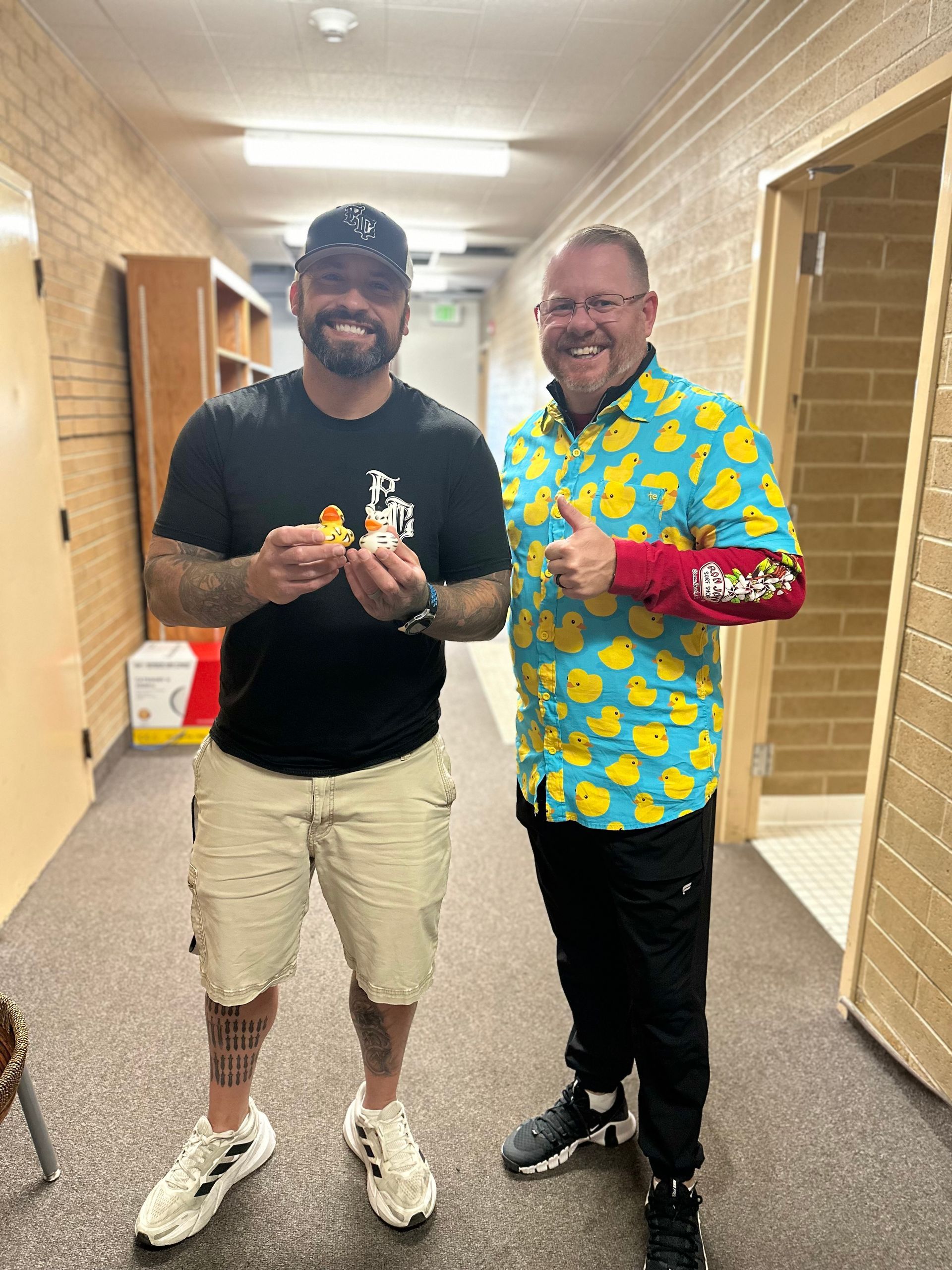 Two men are standing next to each other in a hallway.