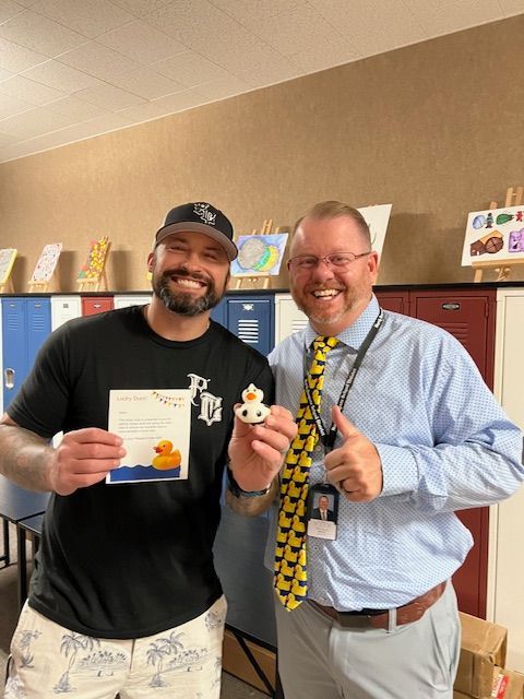 Two men are standing next to each other holding a rubber duck and a certificate.