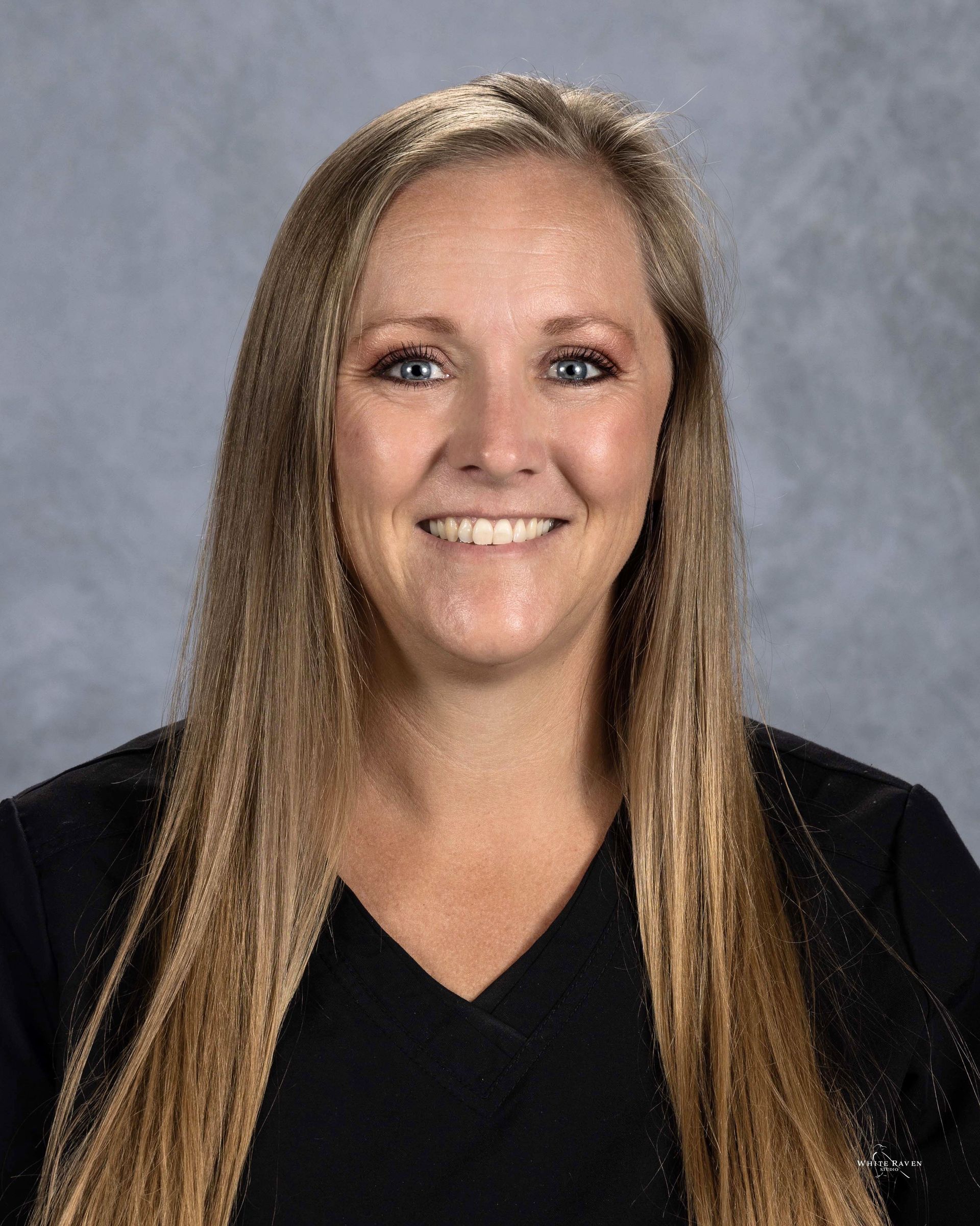 A woman with long blonde hair is wearing a black shirt and smiling for the camera.
