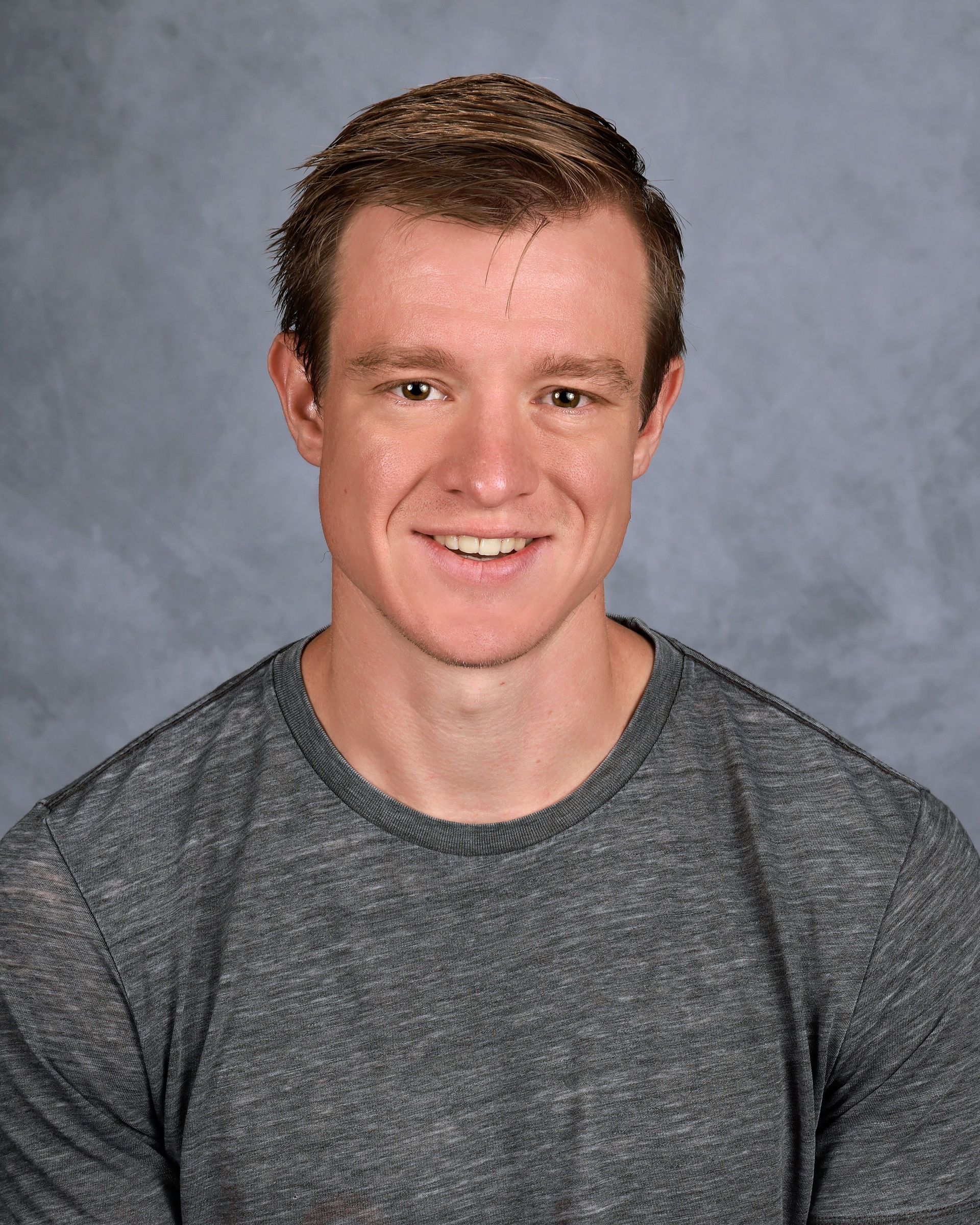 Smiling person in a gray shirt against a mottled gray studio backdrop