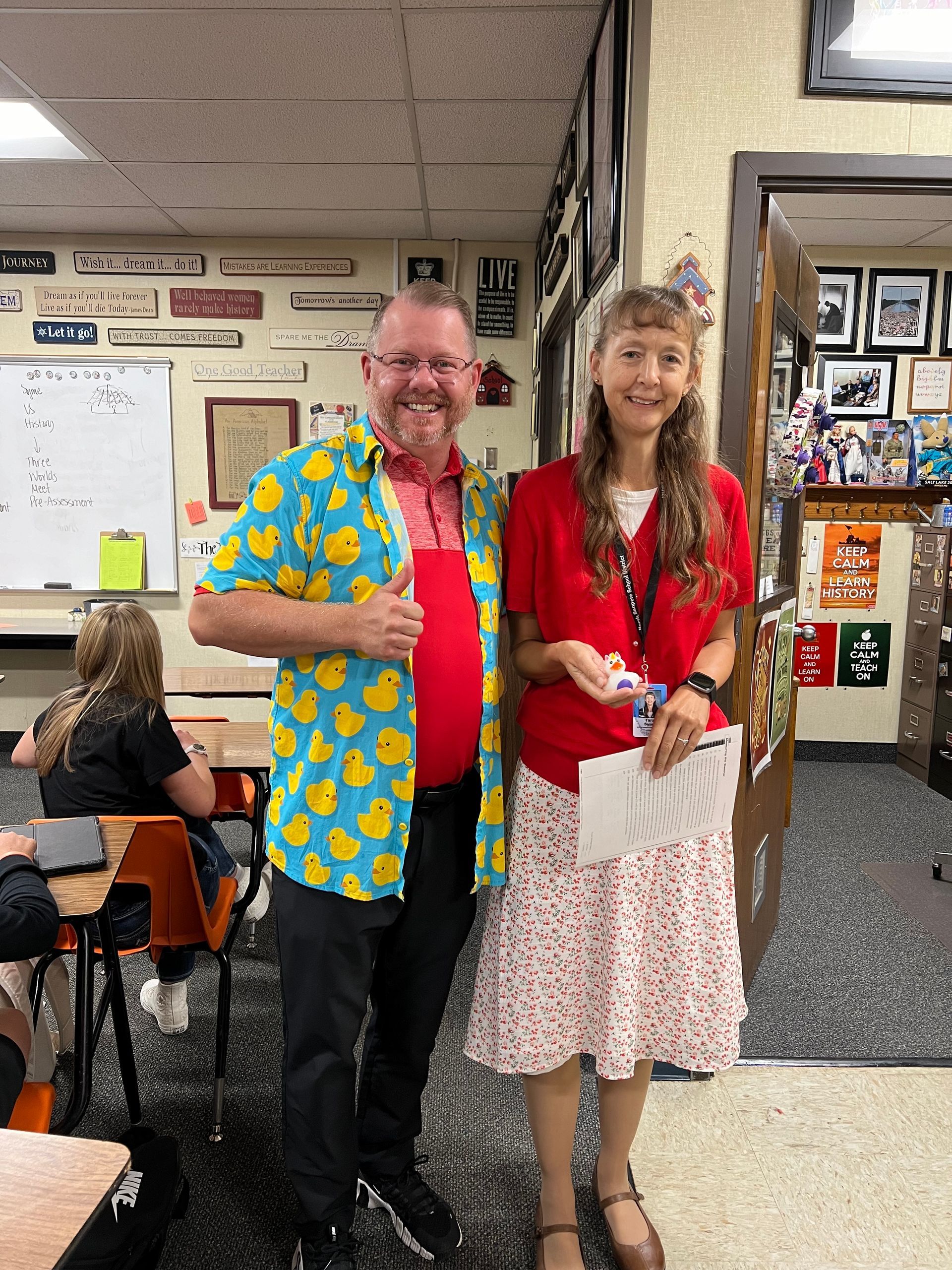 A man and a woman are posing for a picture in a classroom.