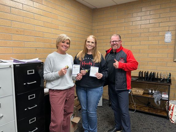 Three people posing with small cups in a brick-walled office break room