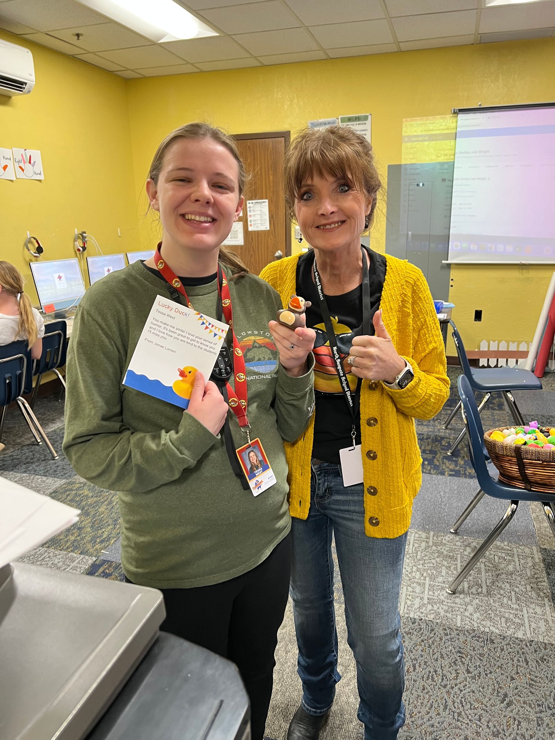 Two women are standing next to each other in a classroom holding cupcakes.