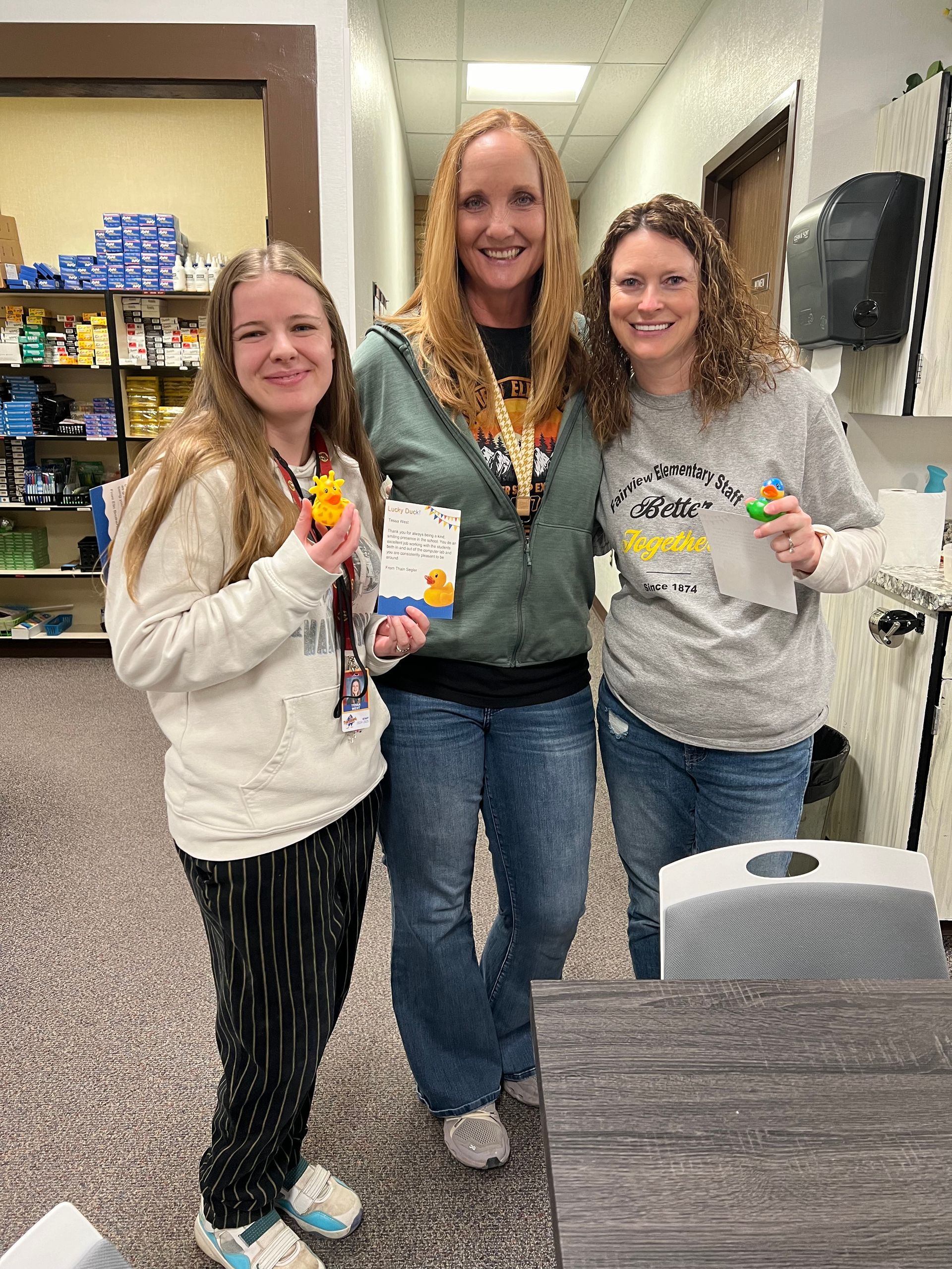 Three women are standing next to each other in a hallway holding toys.