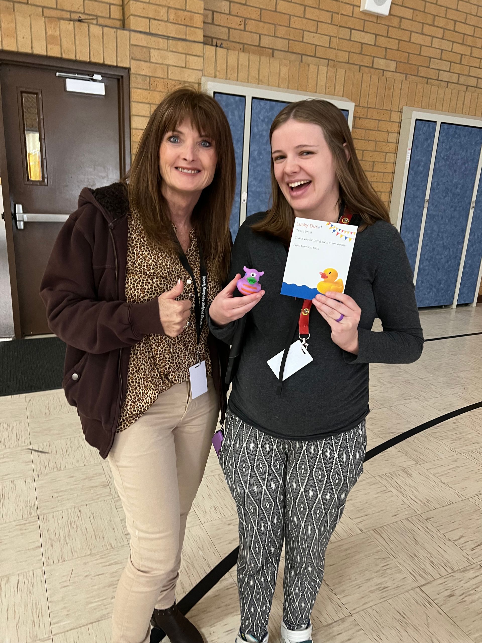 Two women are standing next to each other holding a rubber duck and a card.