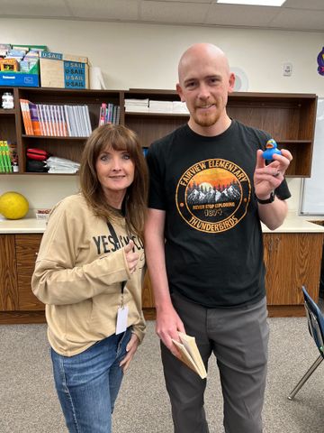 A man and a woman are standing next to each other in a classroom.