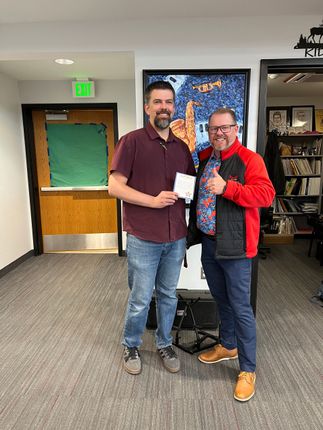 Two people posing indoors, smiling and holding a small white object in front of a TV.