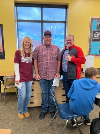 Three people posing indoors in front of a window, one holding a drink and another wearing gloves, with a child seated nearby.
