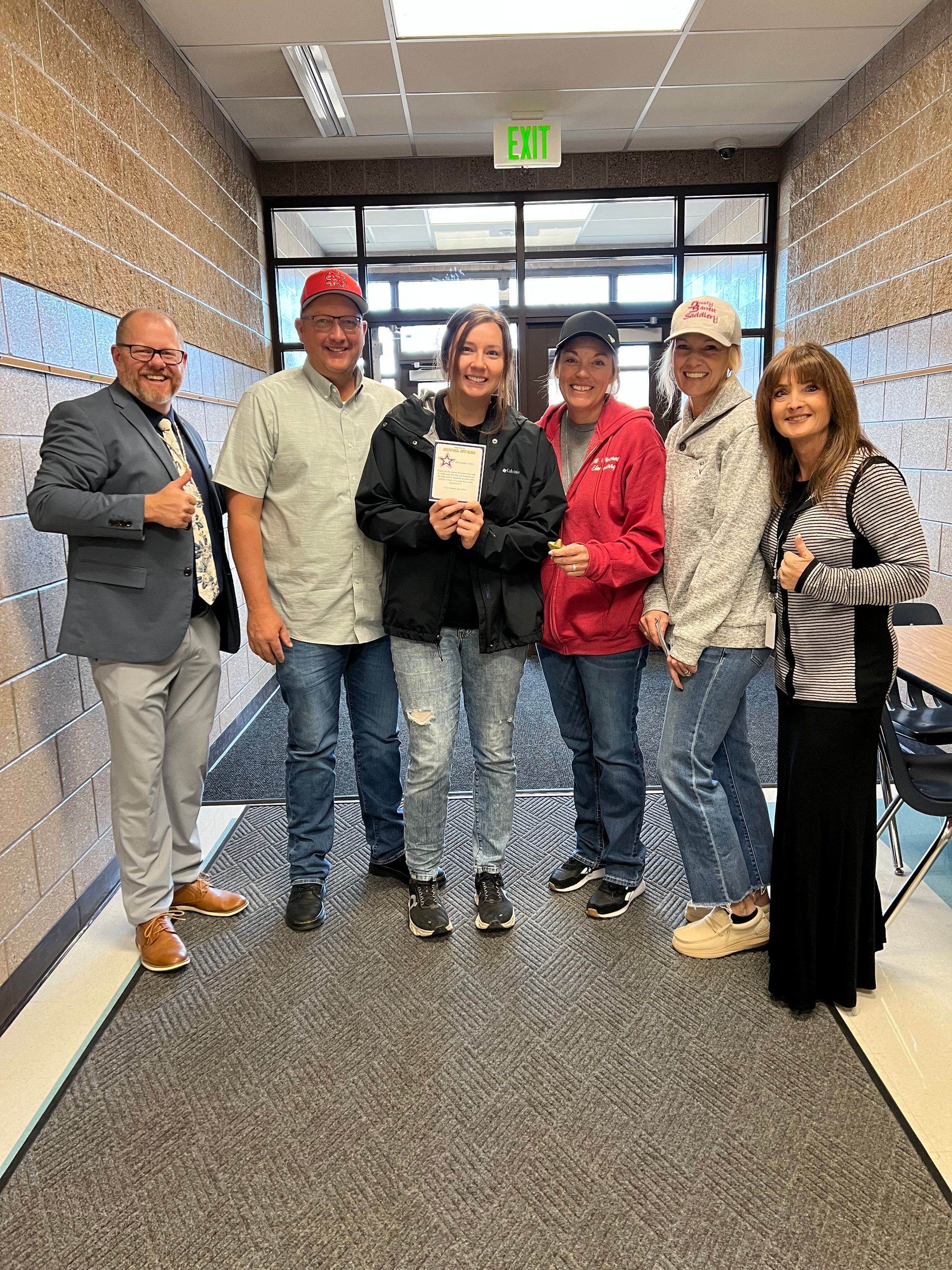 Group of people in a hallway celebrating; a young person holds a document, others wear hats.