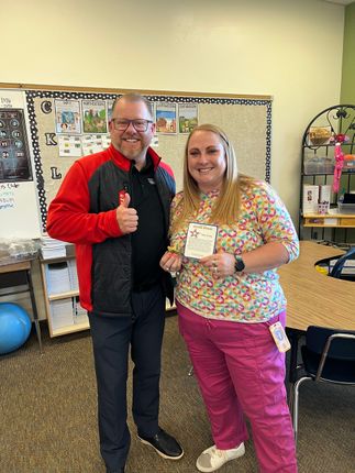 Two people smiling in a classroom, holding a gift and giving thumbs up.