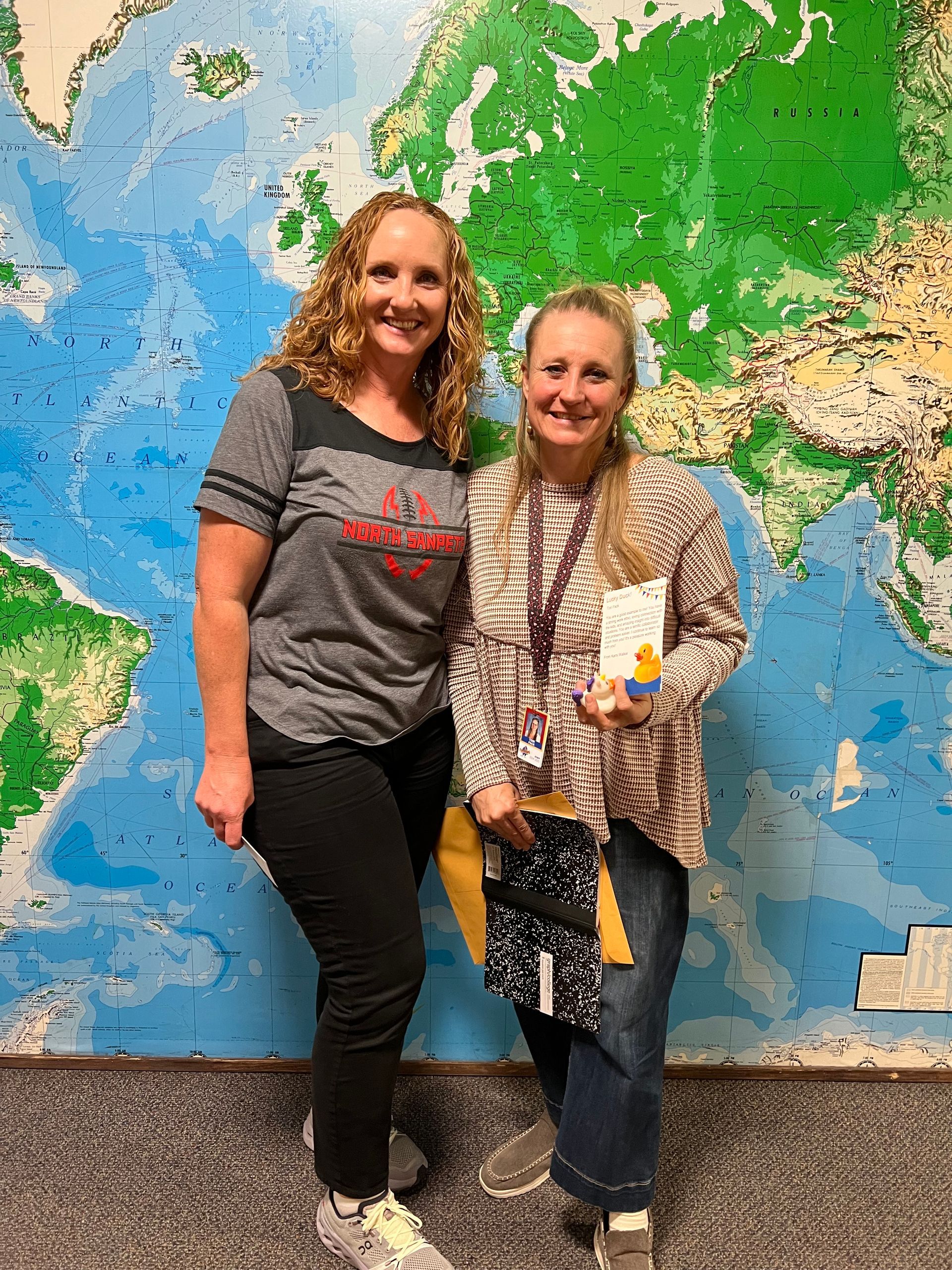 Two women are standing next to each other in front of a large map of the world.