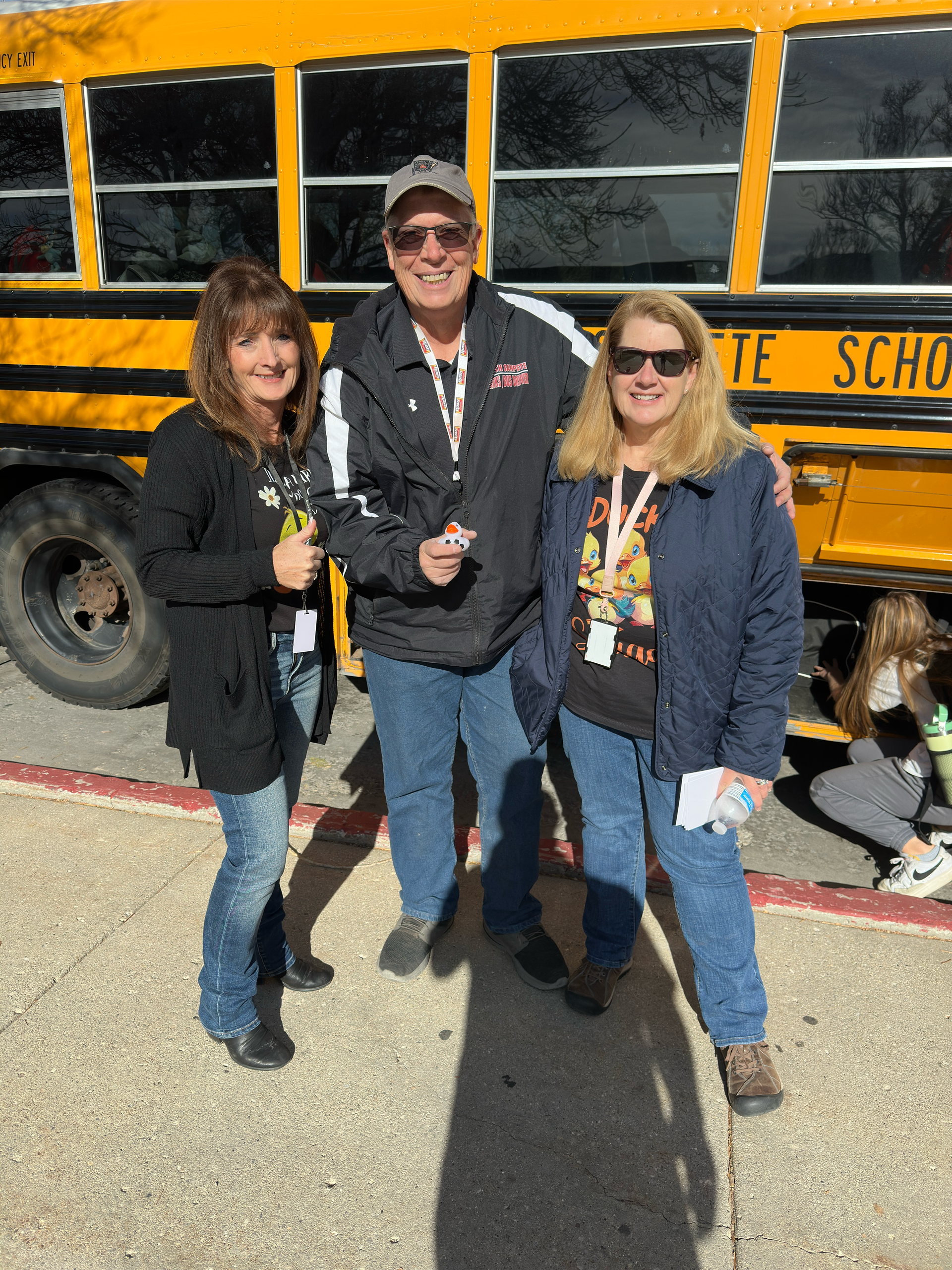 Three people are posing for a picture in front of a school bus.