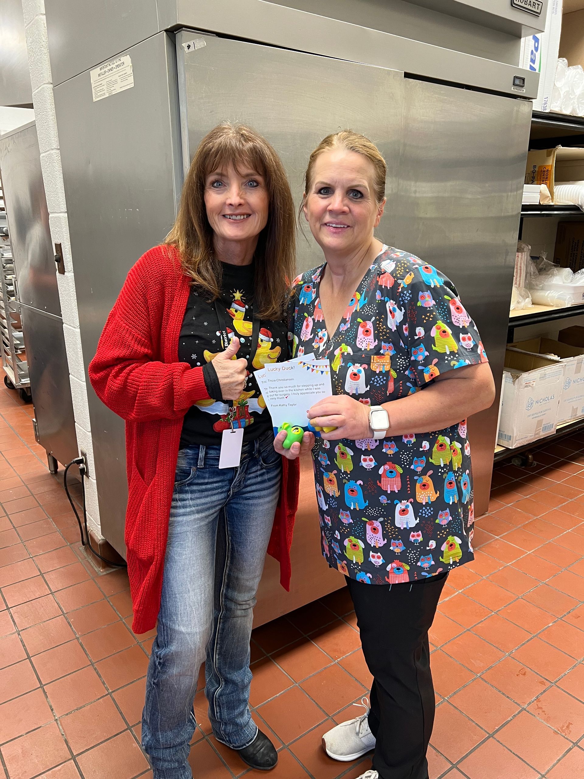 Two women are standing next to each other in a kitchen holding a check.