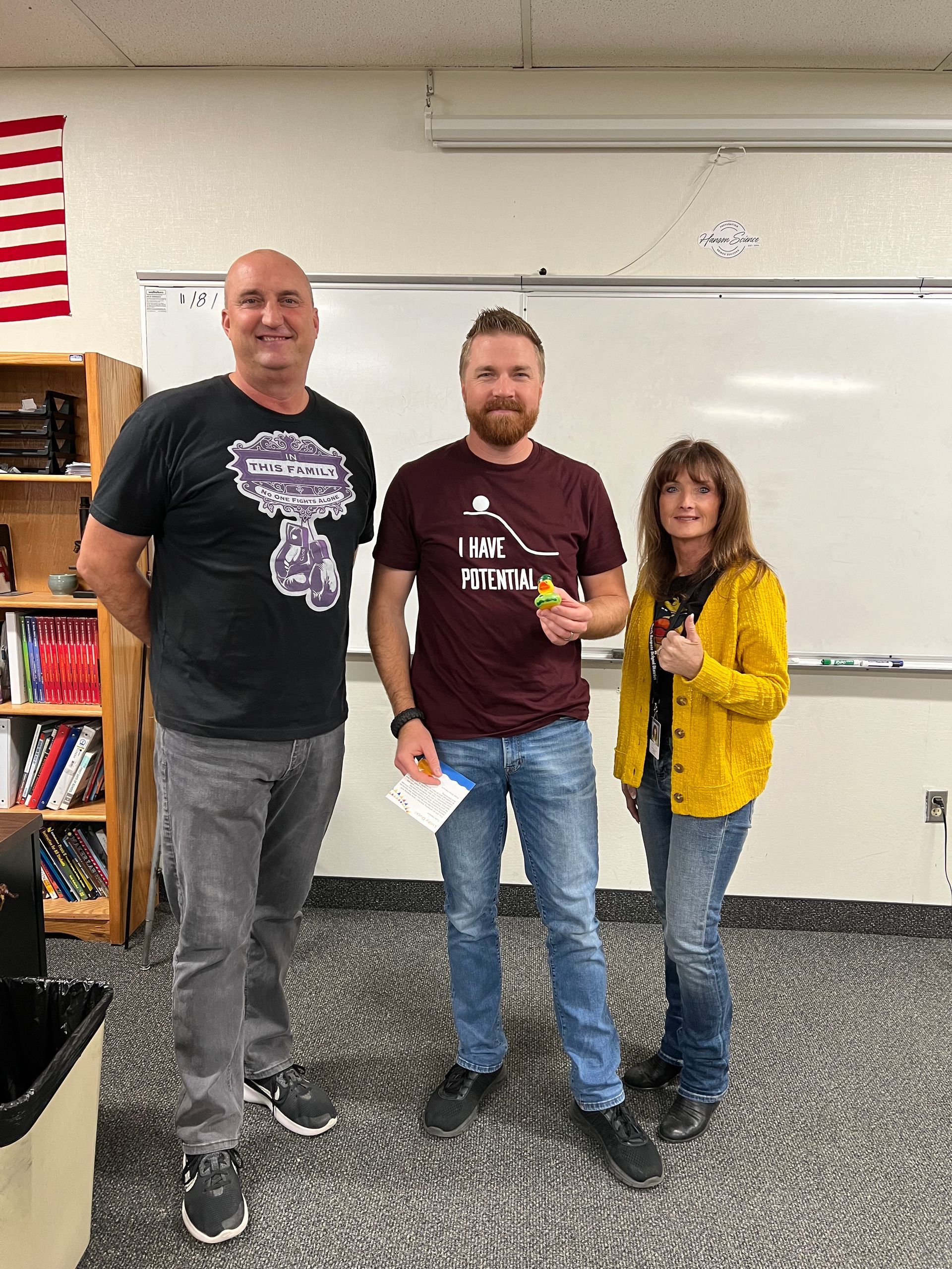 Three people are standing in front of a whiteboard in a classroom.