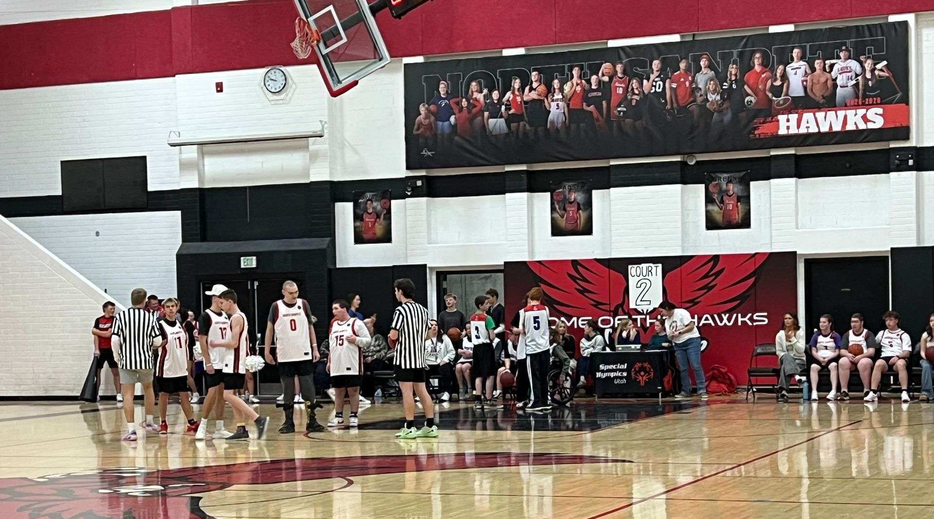 Basketball game in progress; players in uniforms on court, Hawks banner in background.
