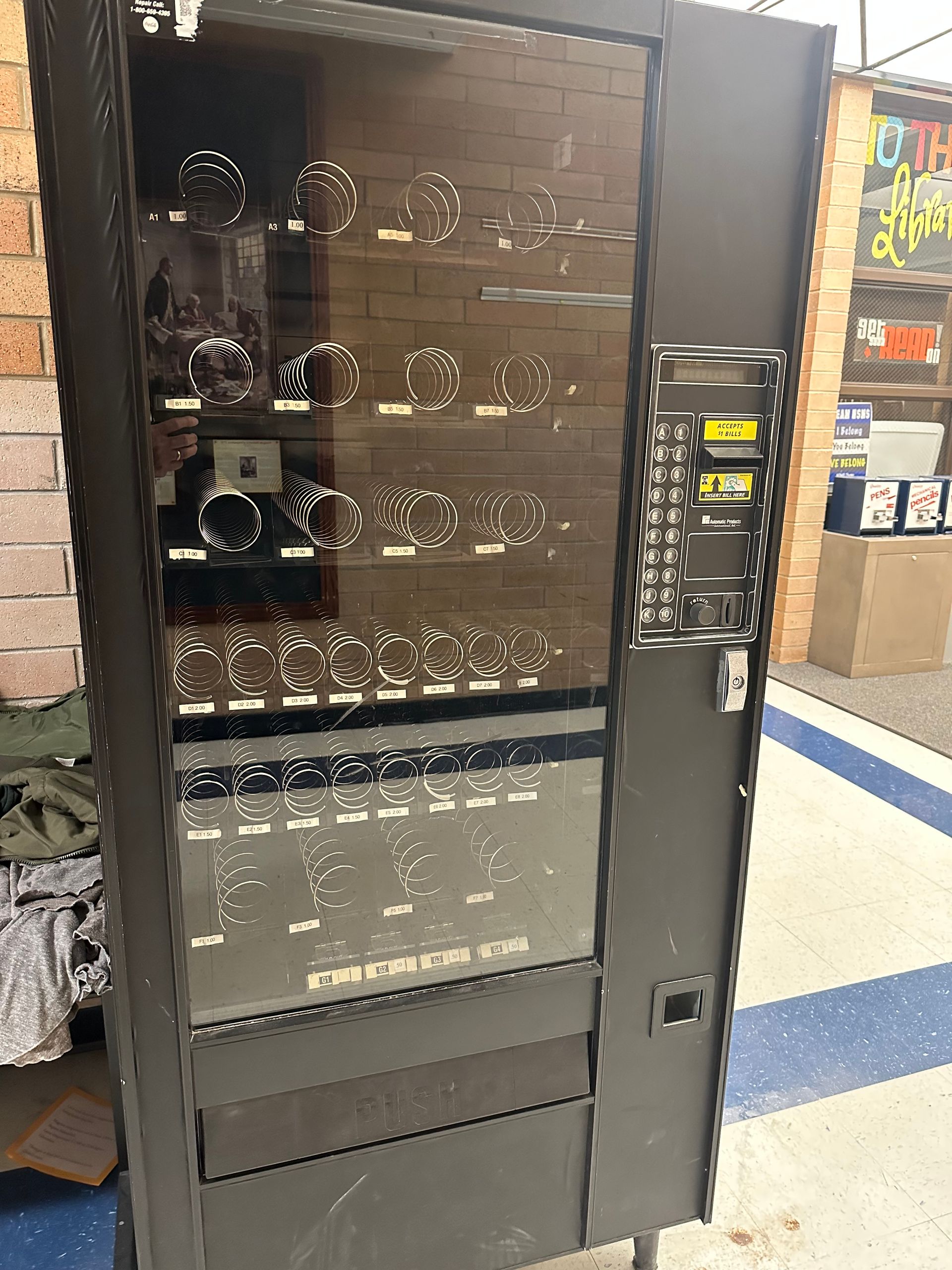 A vending machine is sitting in a room next to a brick wall.