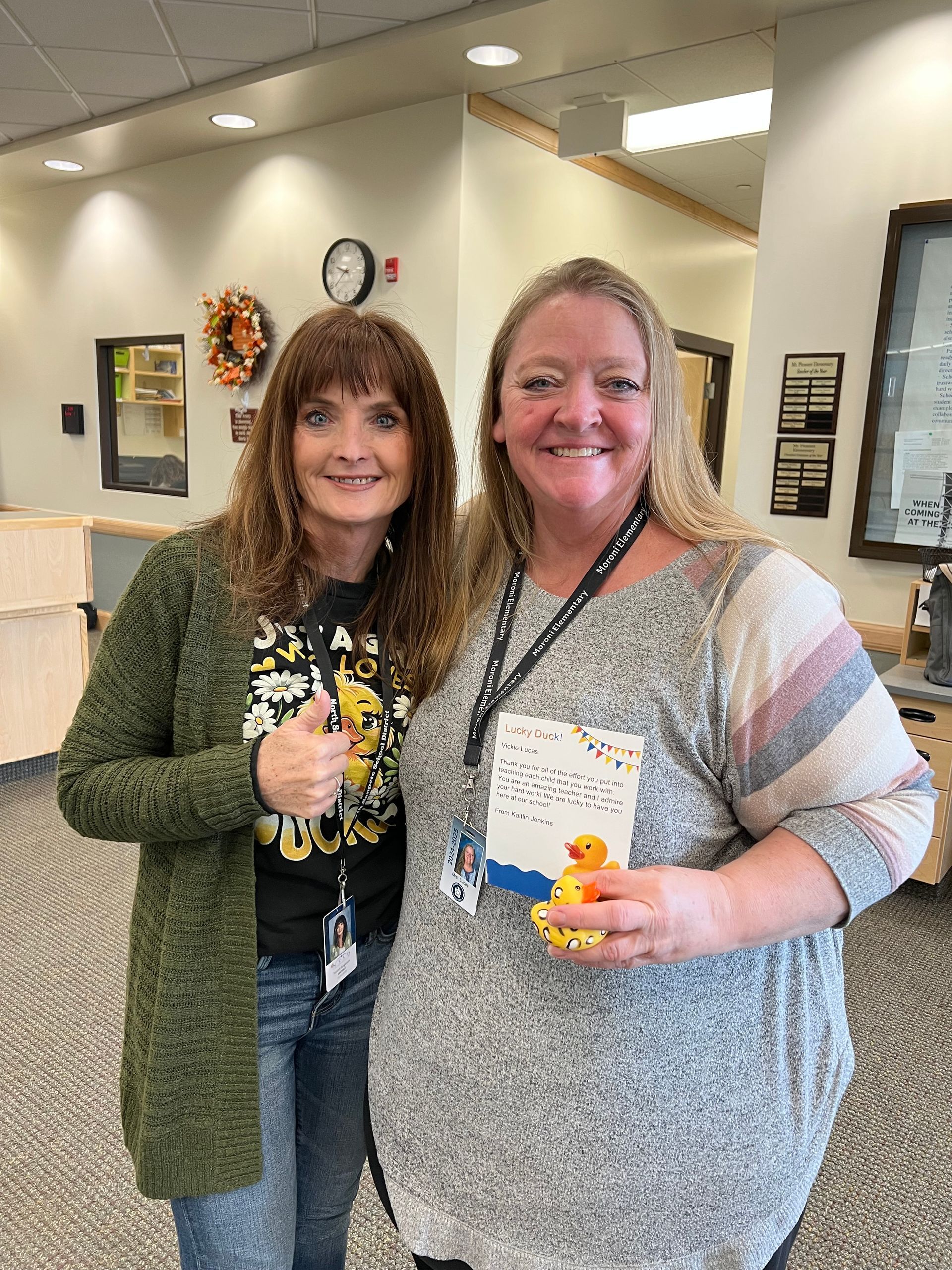 Two women are standing next to each other in a room holding a rubber duck.