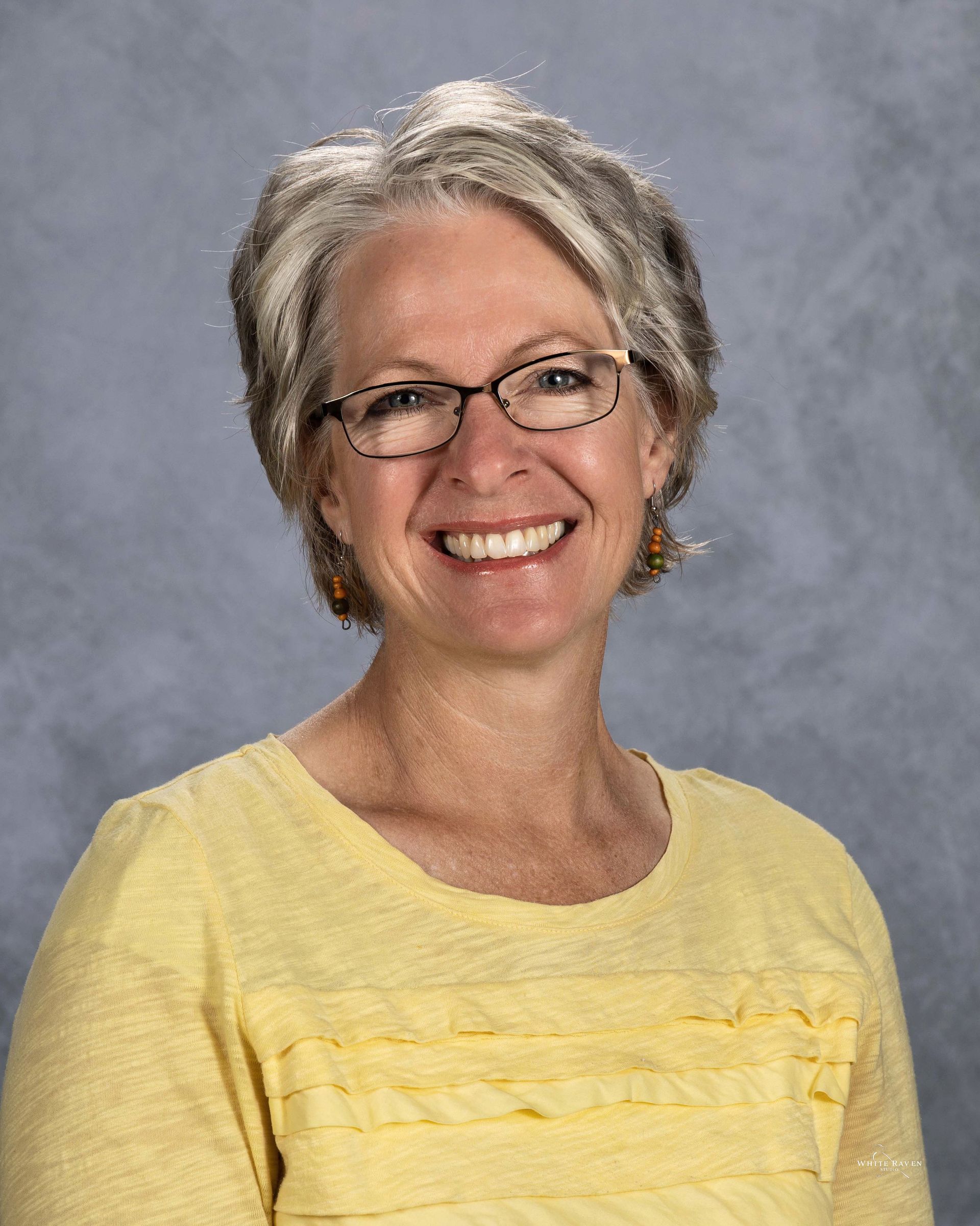 A woman wearing glasses and a yellow shirt is smiling for the camera.