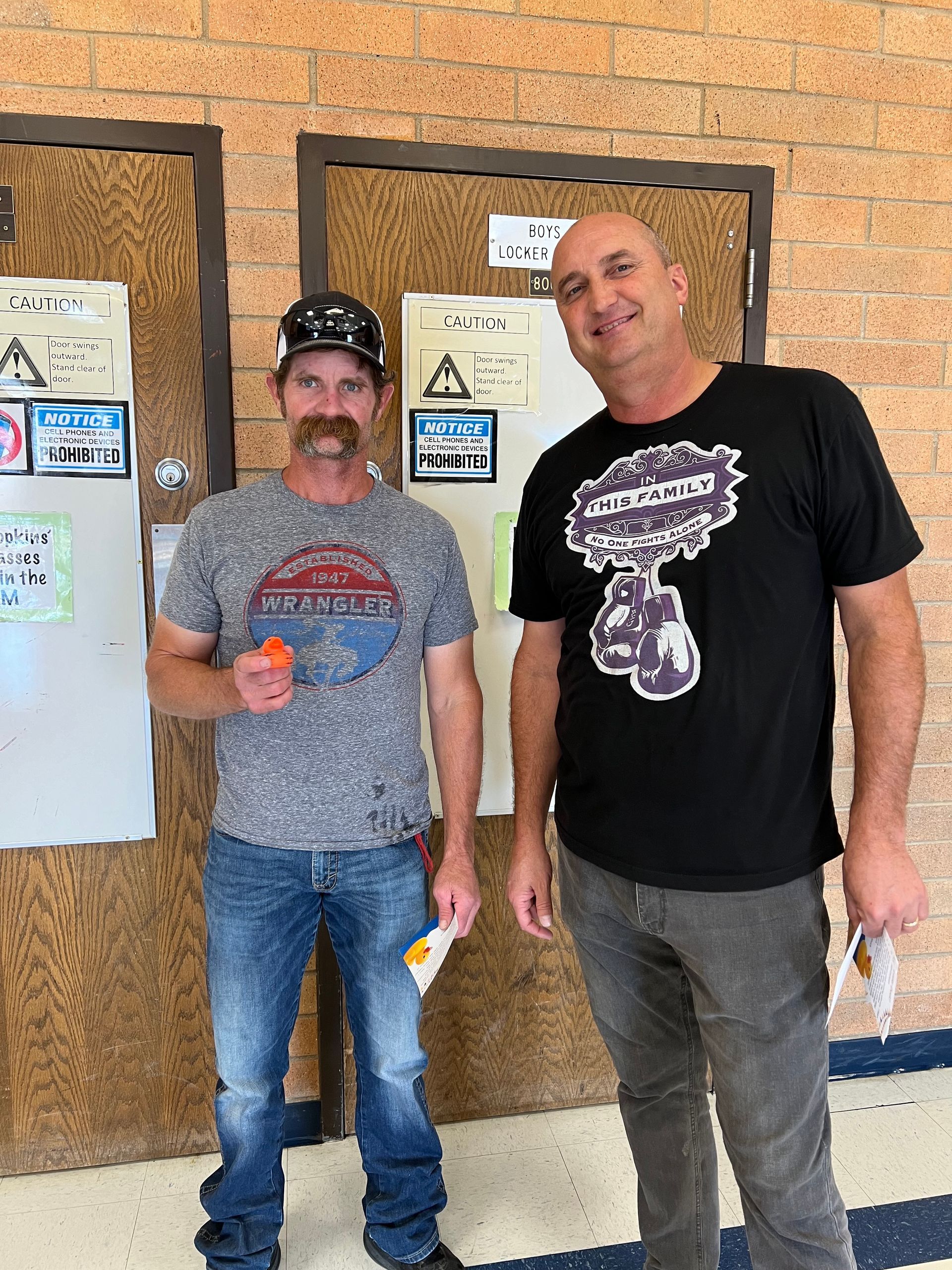 Two men are standing next to each other in front of a brick wall.